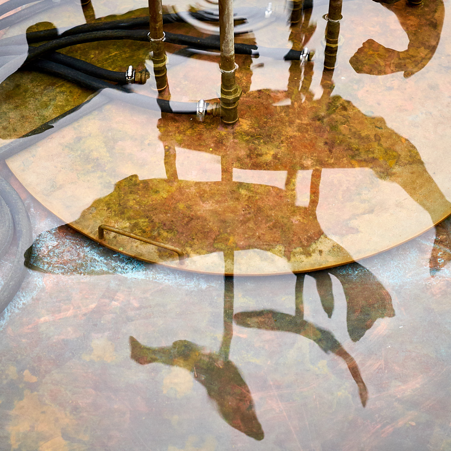 Reflections of metal pipes and a horse figure on water surface.