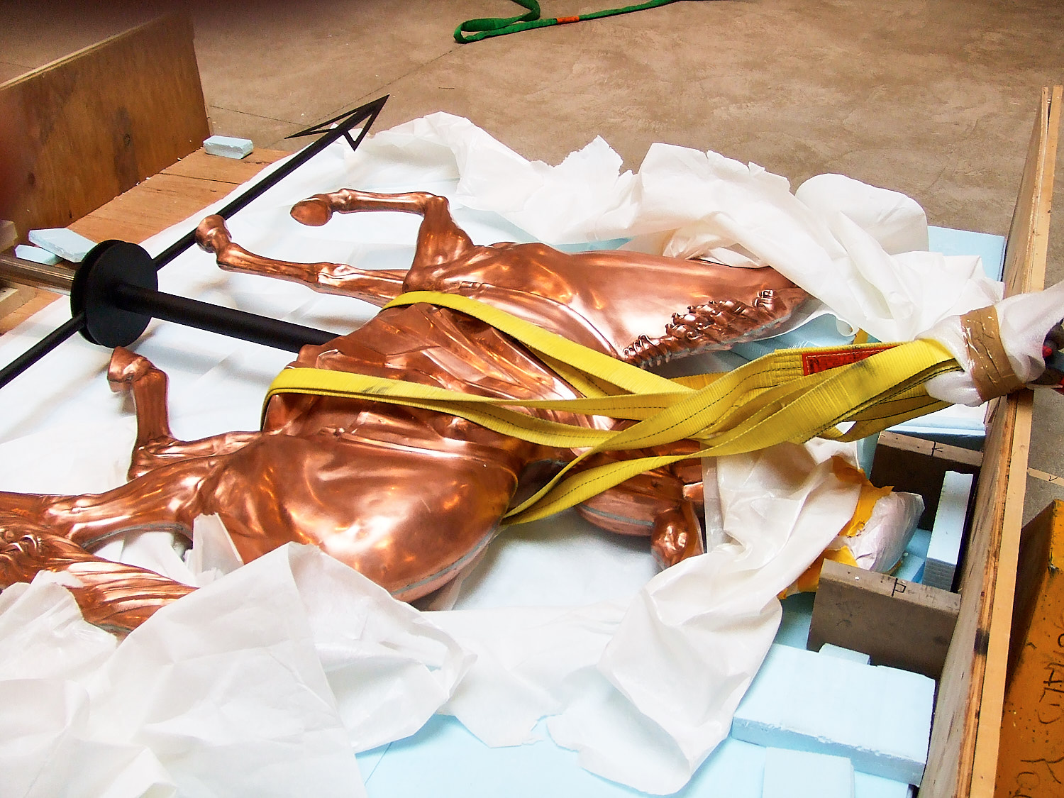 Copper horse weathervane sculpture secured with straps in a wooden crate with packing materials.