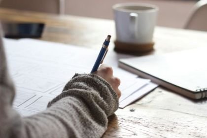 Link to Reviews page - close up of a hand writing on a desk
