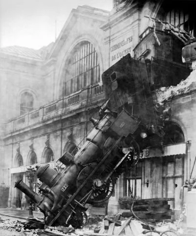 Old black and white photo of a steam train which has gone through a wall and fallen out of a station onto the street below