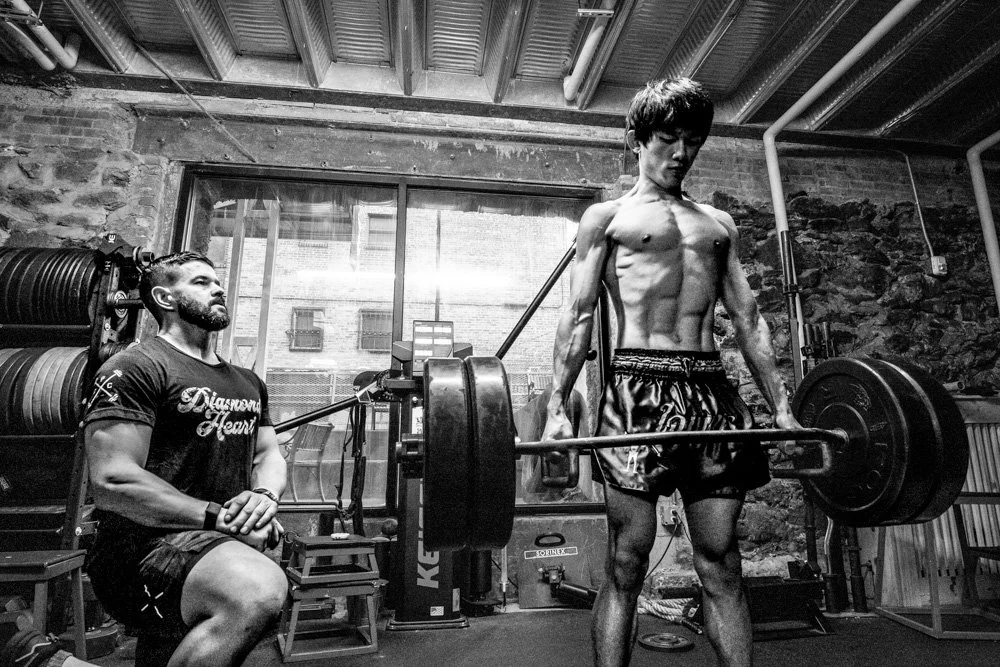 Man deadlifting heavy weights in a gym with a trainer watching