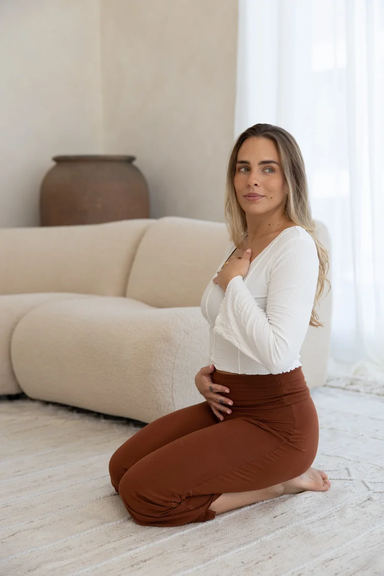 Mara kneeling on a rug at home, one hand on her chest and one on her belly