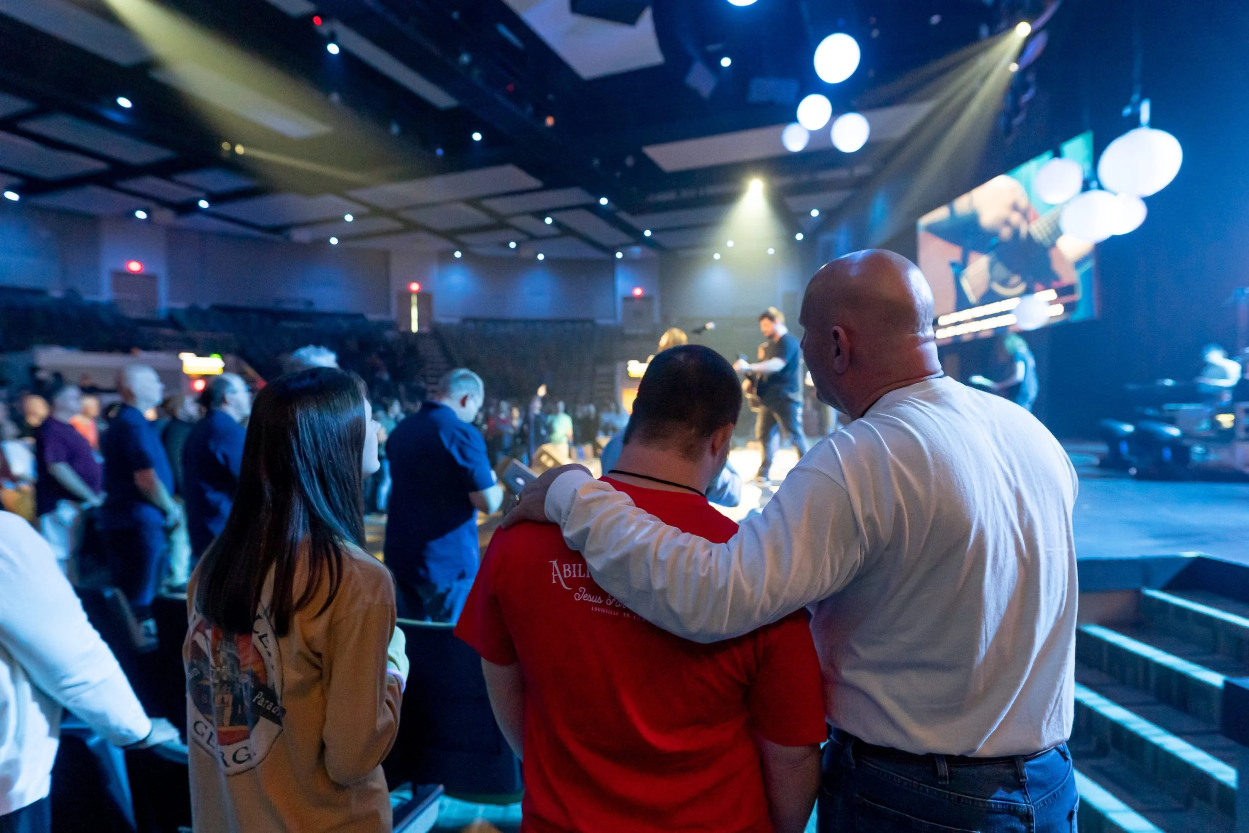 Man with his arm around another man in a worship service.