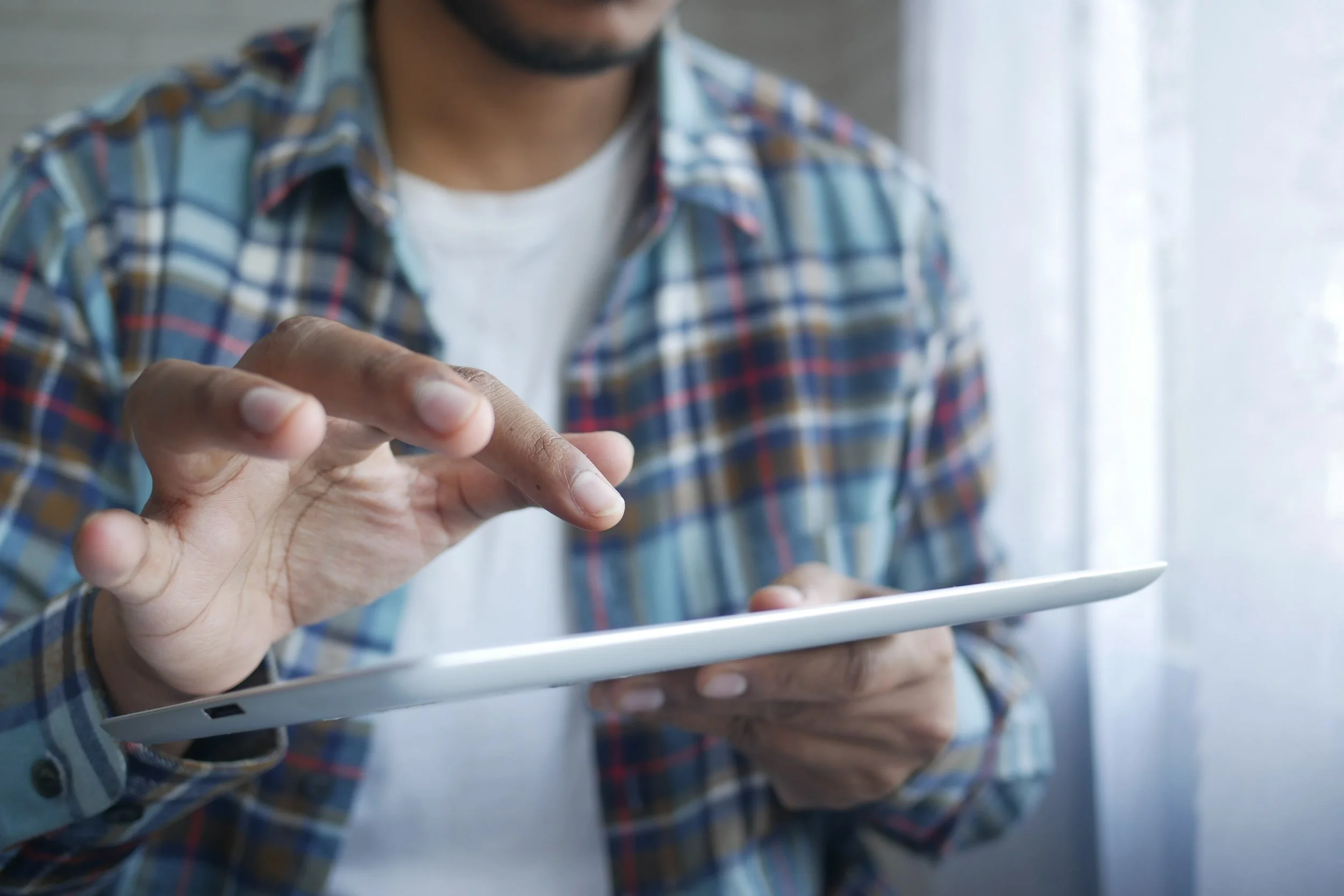 Image of a man holding a tablet and in position to press a button on the screen.