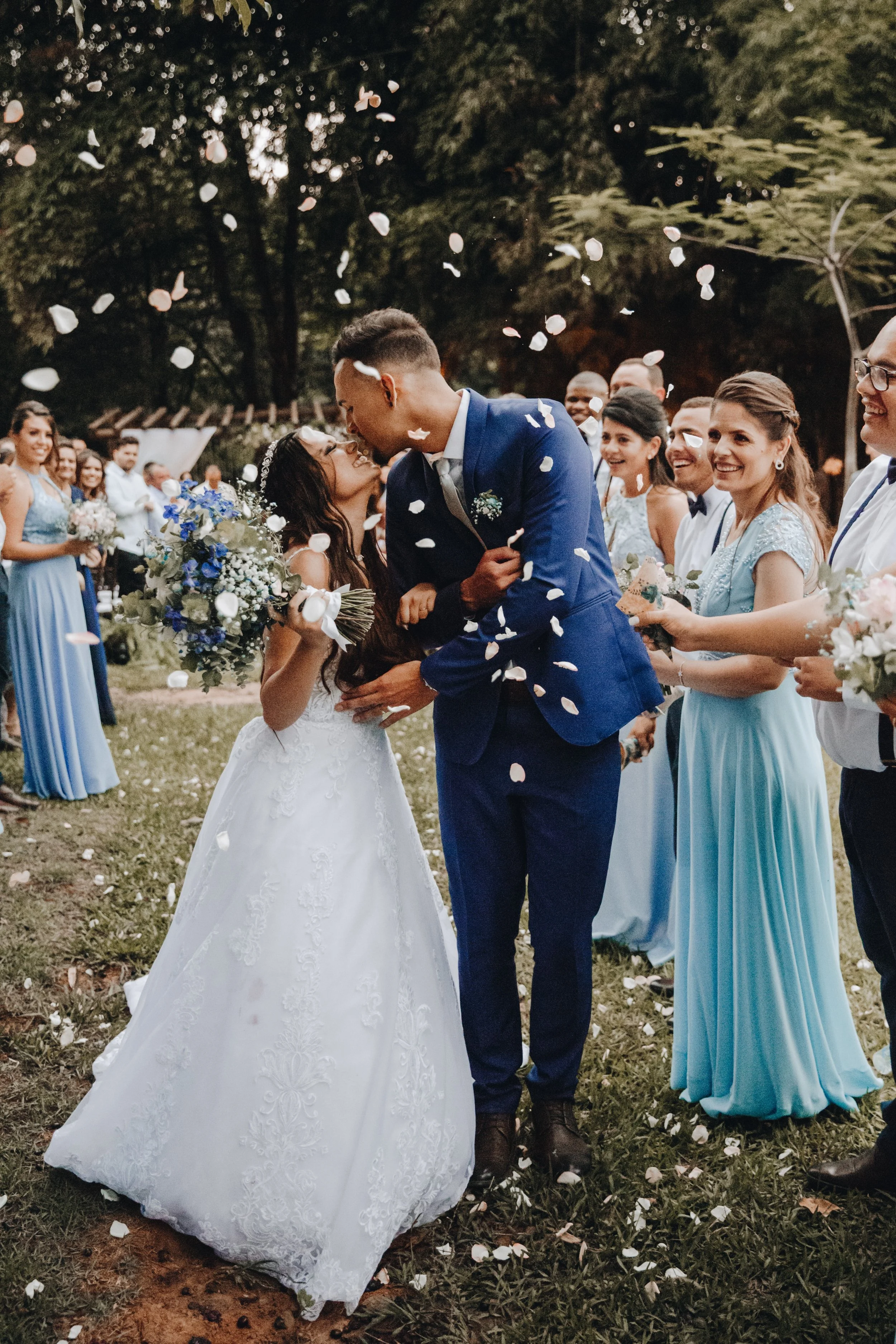 Bride and groom smiling at each other while guests throw rose petals at them