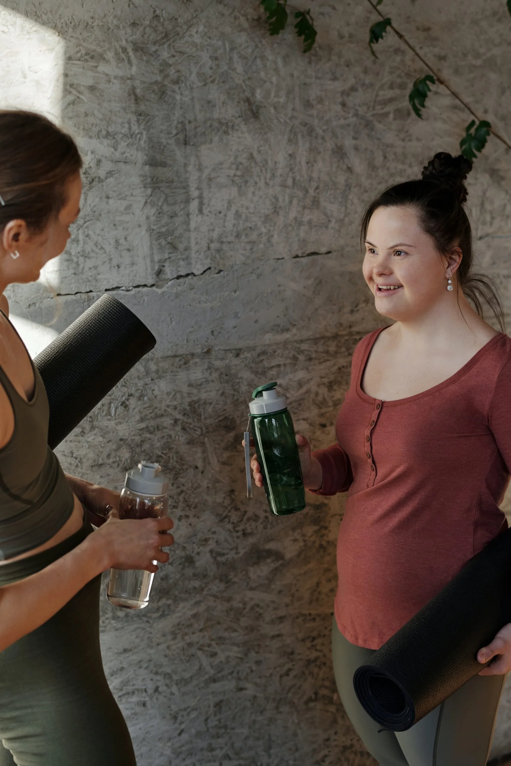 Two women holding yoga mats and talking to each other