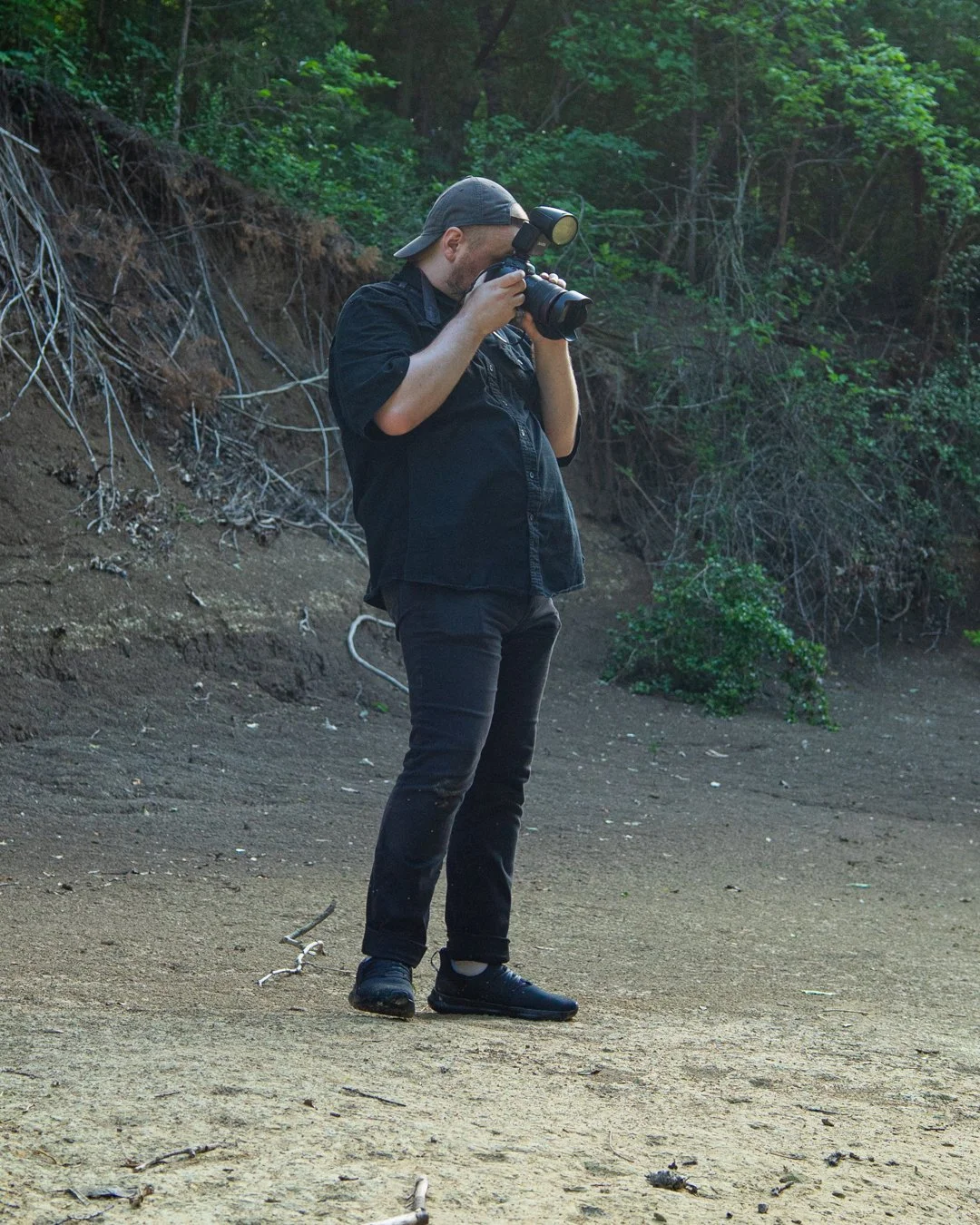 Photographer standing on the bank of a creek, holding a camera and looking for the shot.