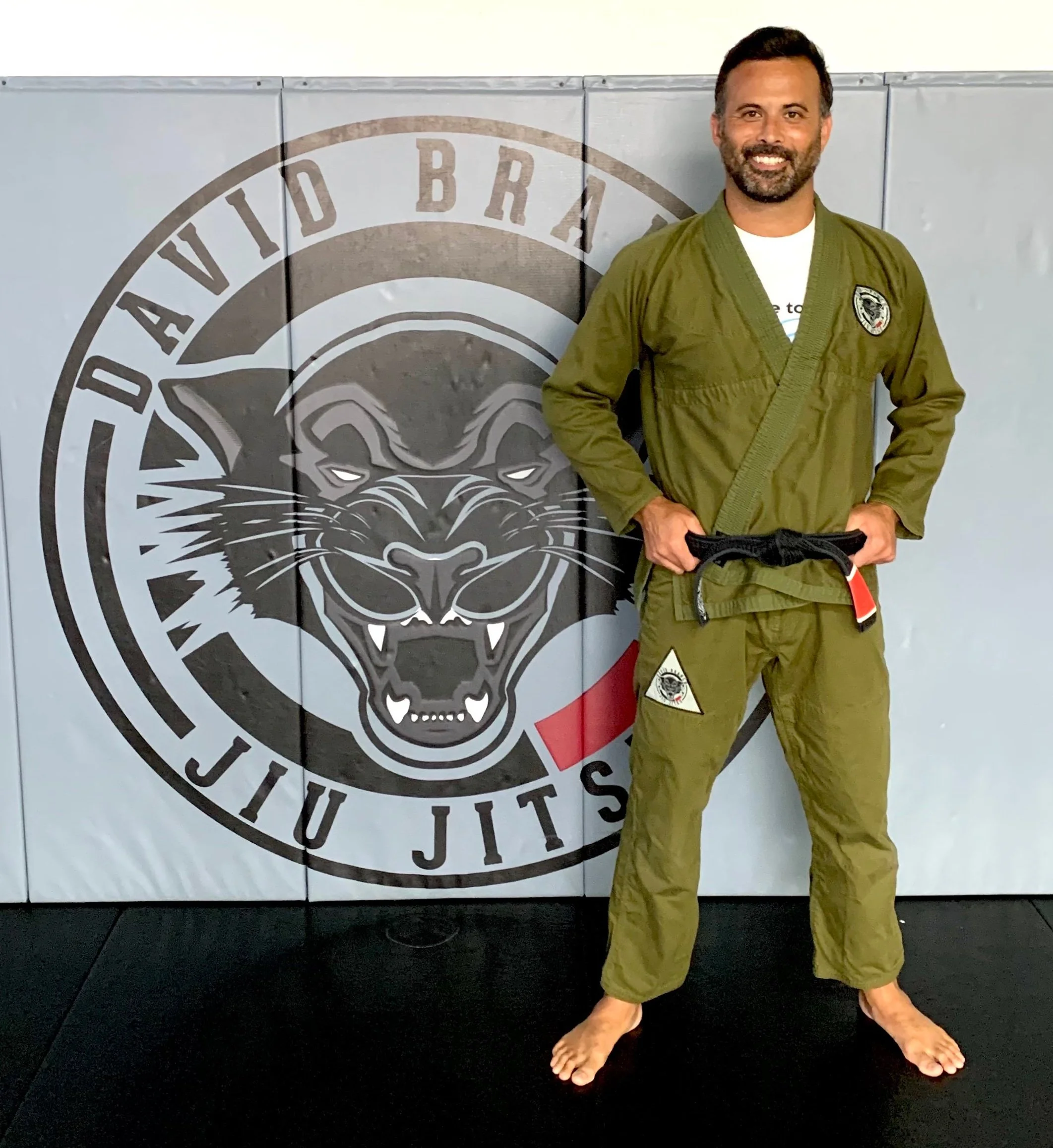 Professor Matt Loy standing in front of the David Branch Jiu Jitsu logo inside the gym.