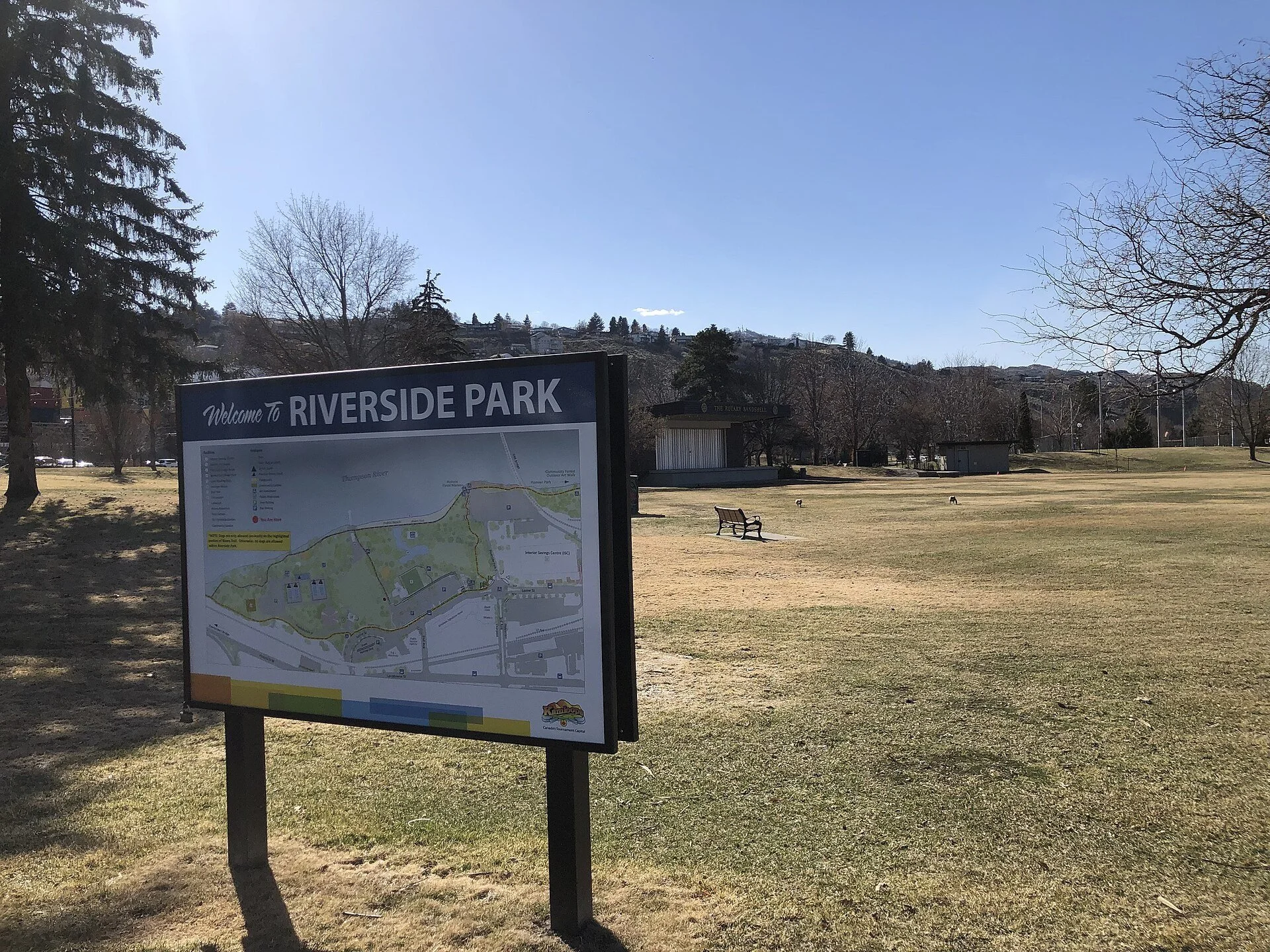 A Riverside Park sign and open lawn with trees in downtown Kamloops, BC.