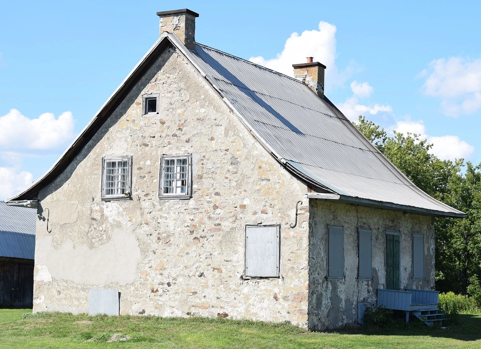 The fieldstone Maison-Brossard farmhouse with a steep metal roof and twin chimneys on chemin des Prairies in Brossard.