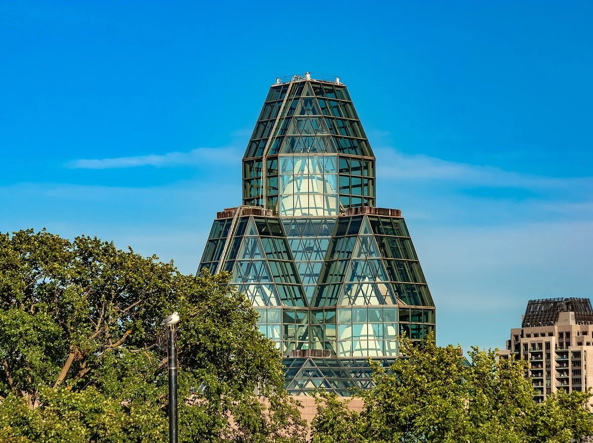 The glass tower of the National Gallery of Canada on Sussex Drive in Ottawa against a blue sky, framed by green trees.