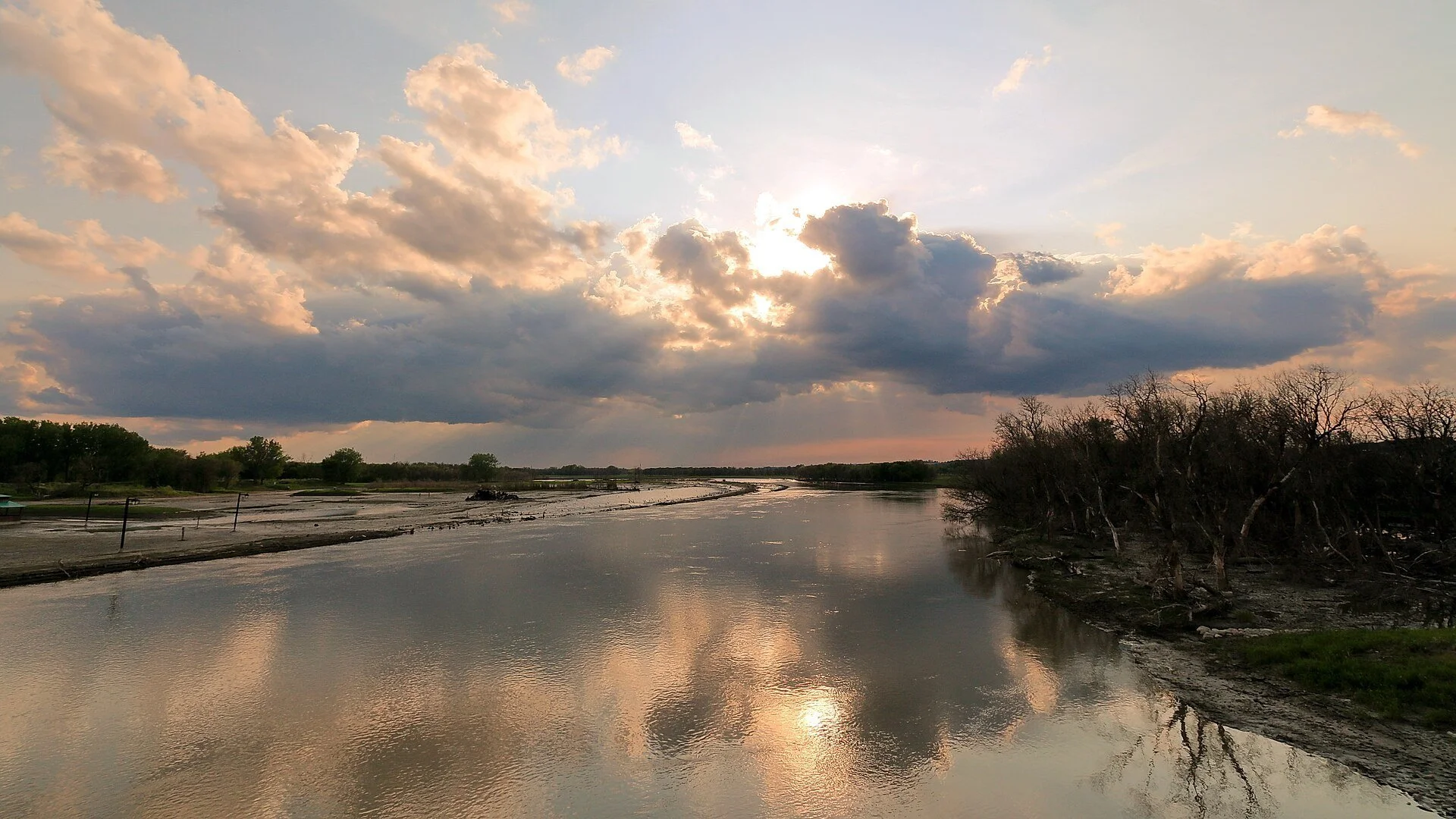 The Assiniboine River in Brandon reflecting a cloudy evening sky between low wooded banks.