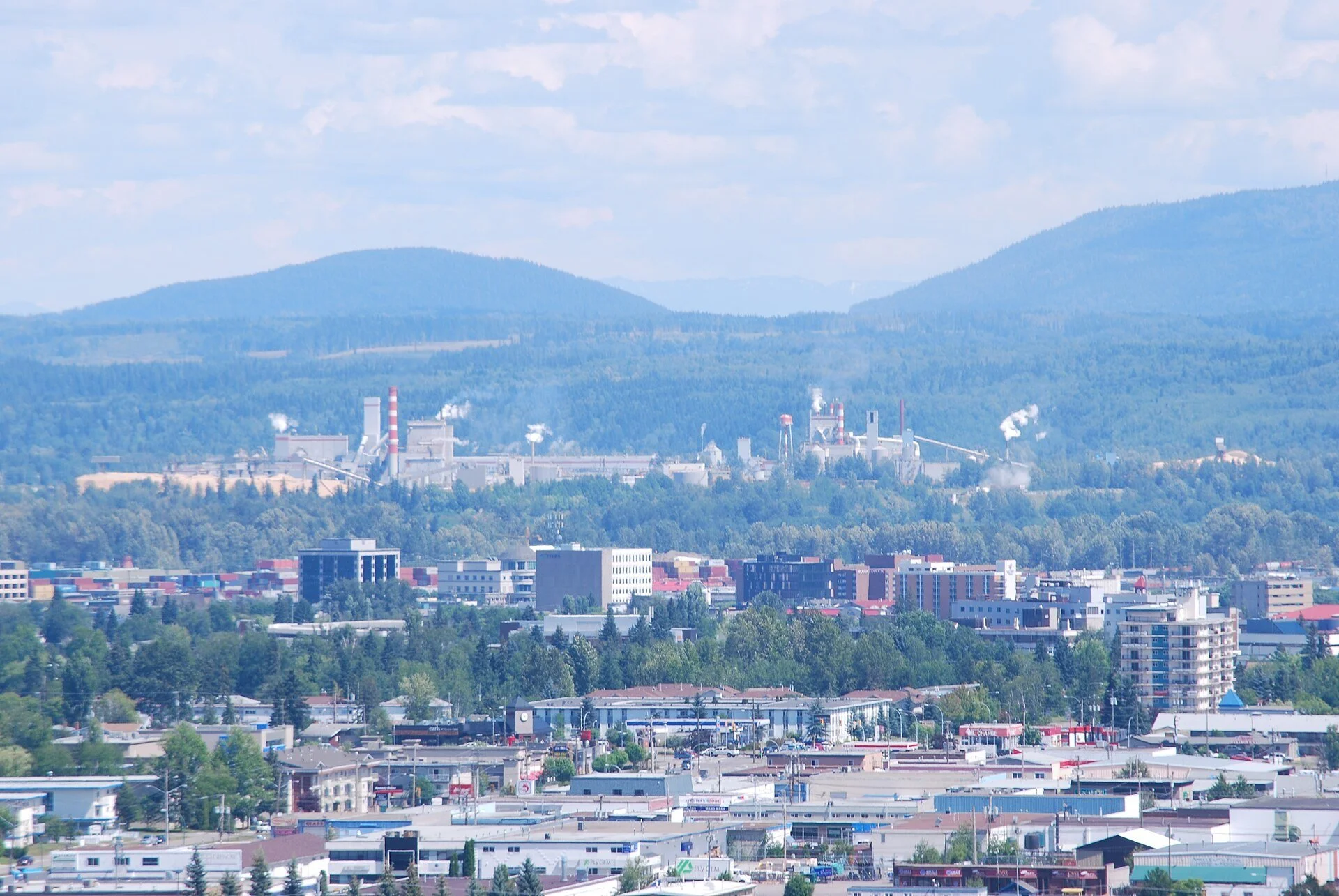 A summer view over downtown Prince George, British Columbia, with forested hills beyond.