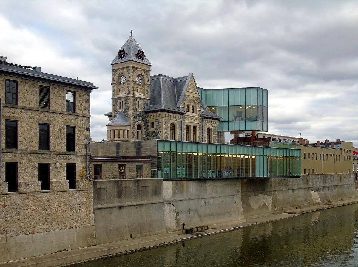 The stone clock tower of the Old Post Office in Cambridge, with its modern glass addition, above the Grand River in downtown Galt.