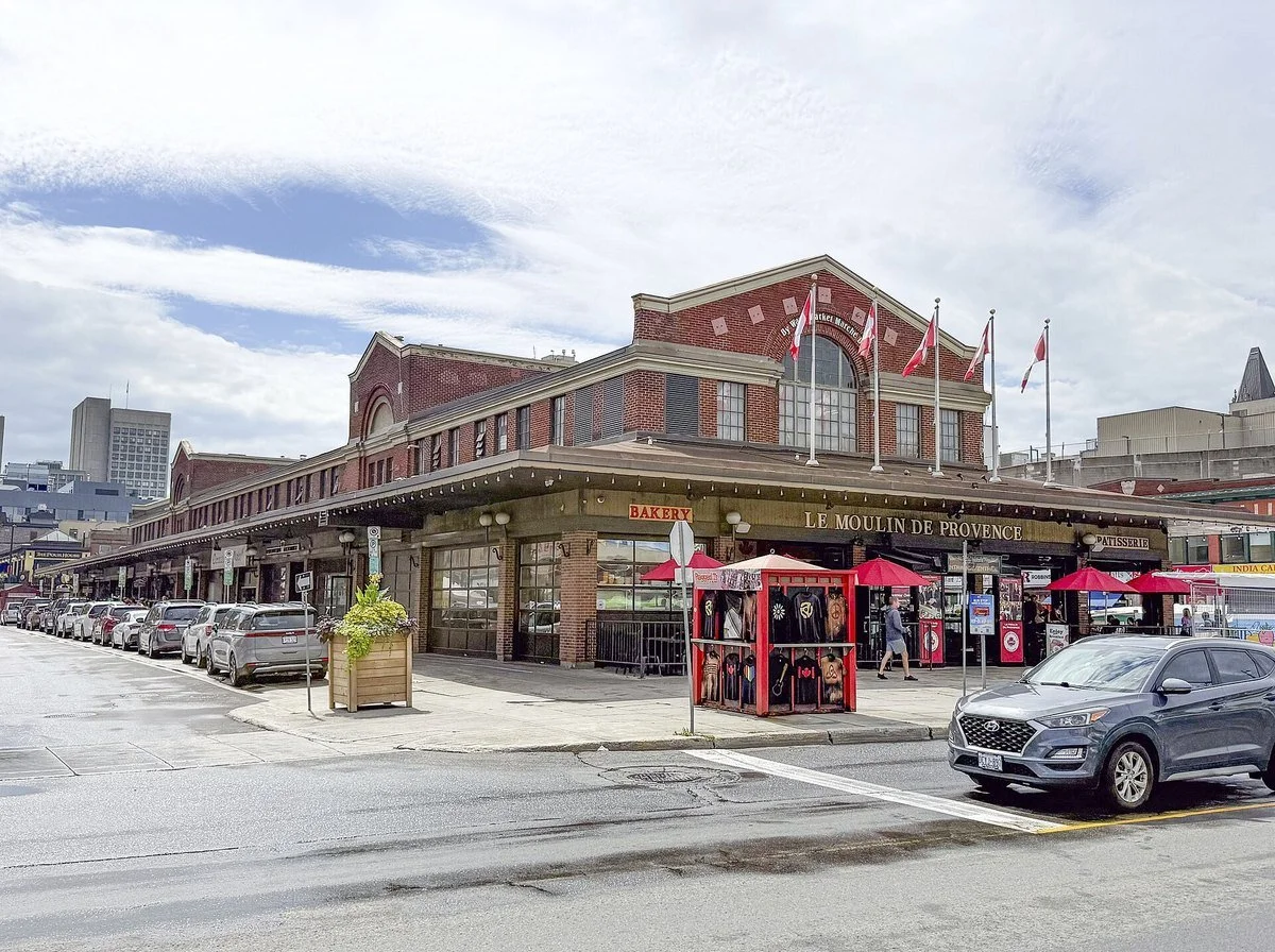 The red brick ByWard Market building in downtown Ottawa, with flags along the roofline and shops at street level.