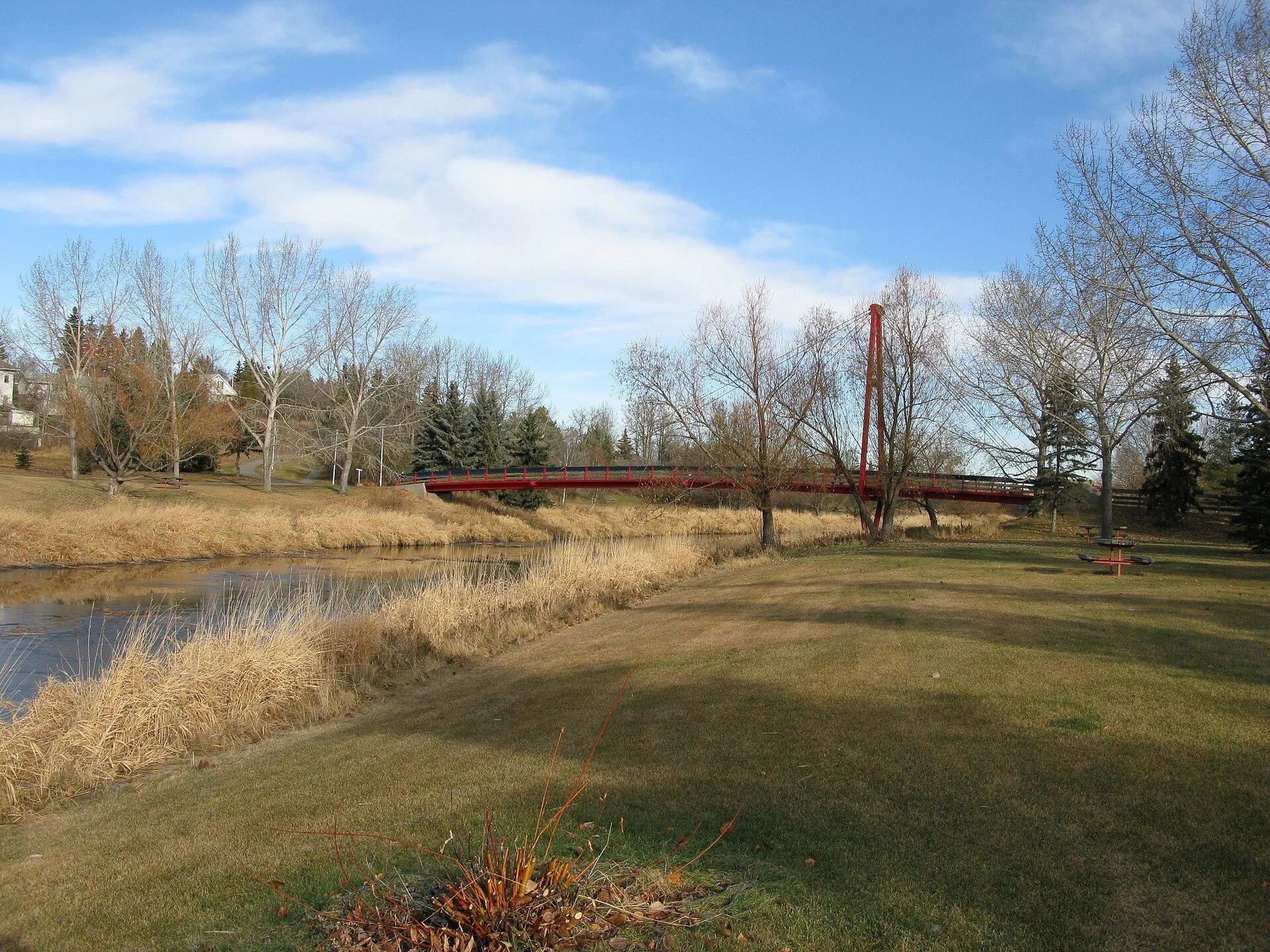 The Sturgeon River in St. Albert with dry grass on the banks, bare trees and a red footbridge.