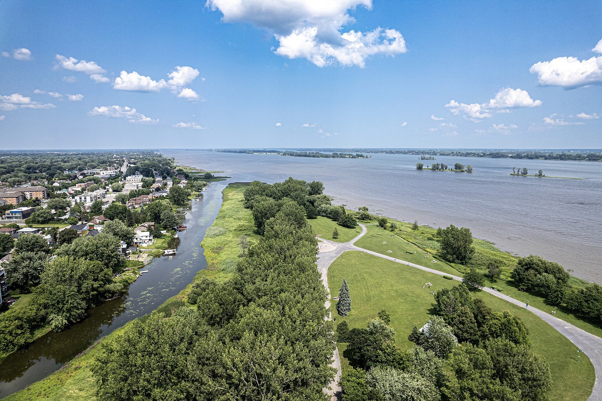 Aerial view of Parc de l'Île-Lebel in Repentigny, with green lawns, trees and a winding path beside the wide St. Lawrence River.