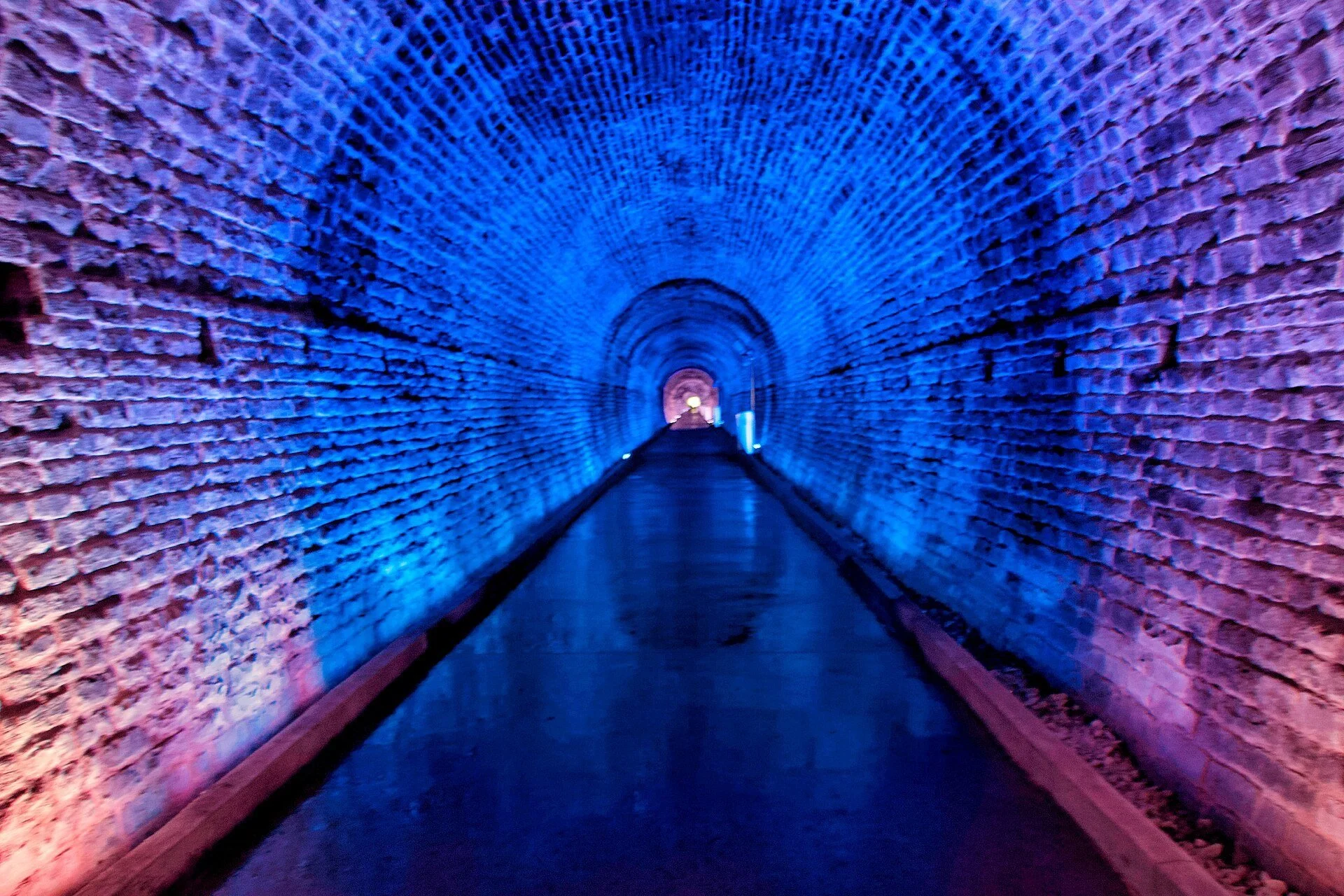 The arched brick interior of the Brockville Railway Tunnel glowing blue and pink under coloured lights.