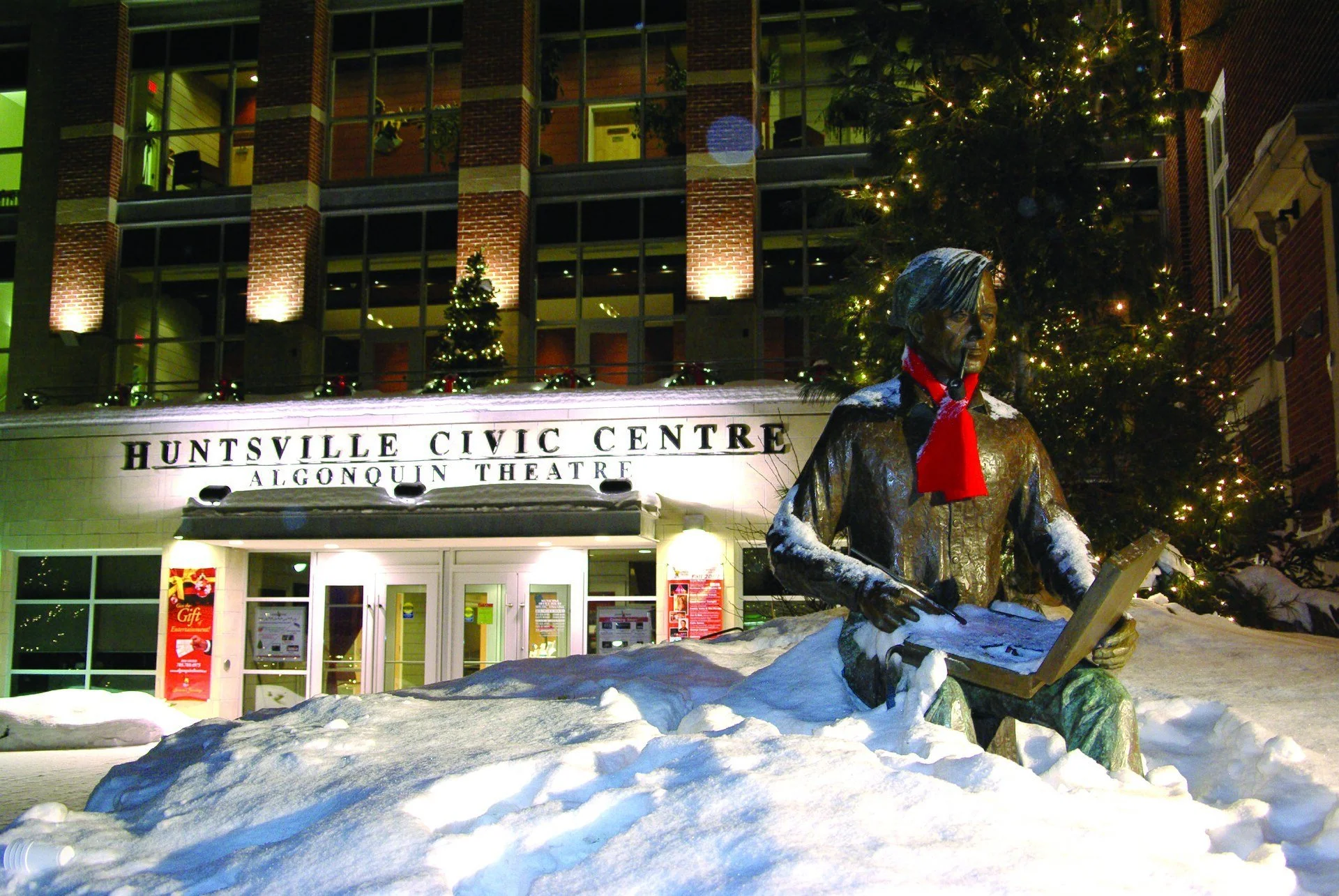 The Huntsville Civic Centre and Algonquin Theatre at night, with the snow-covered Tom Thomson statue in front.