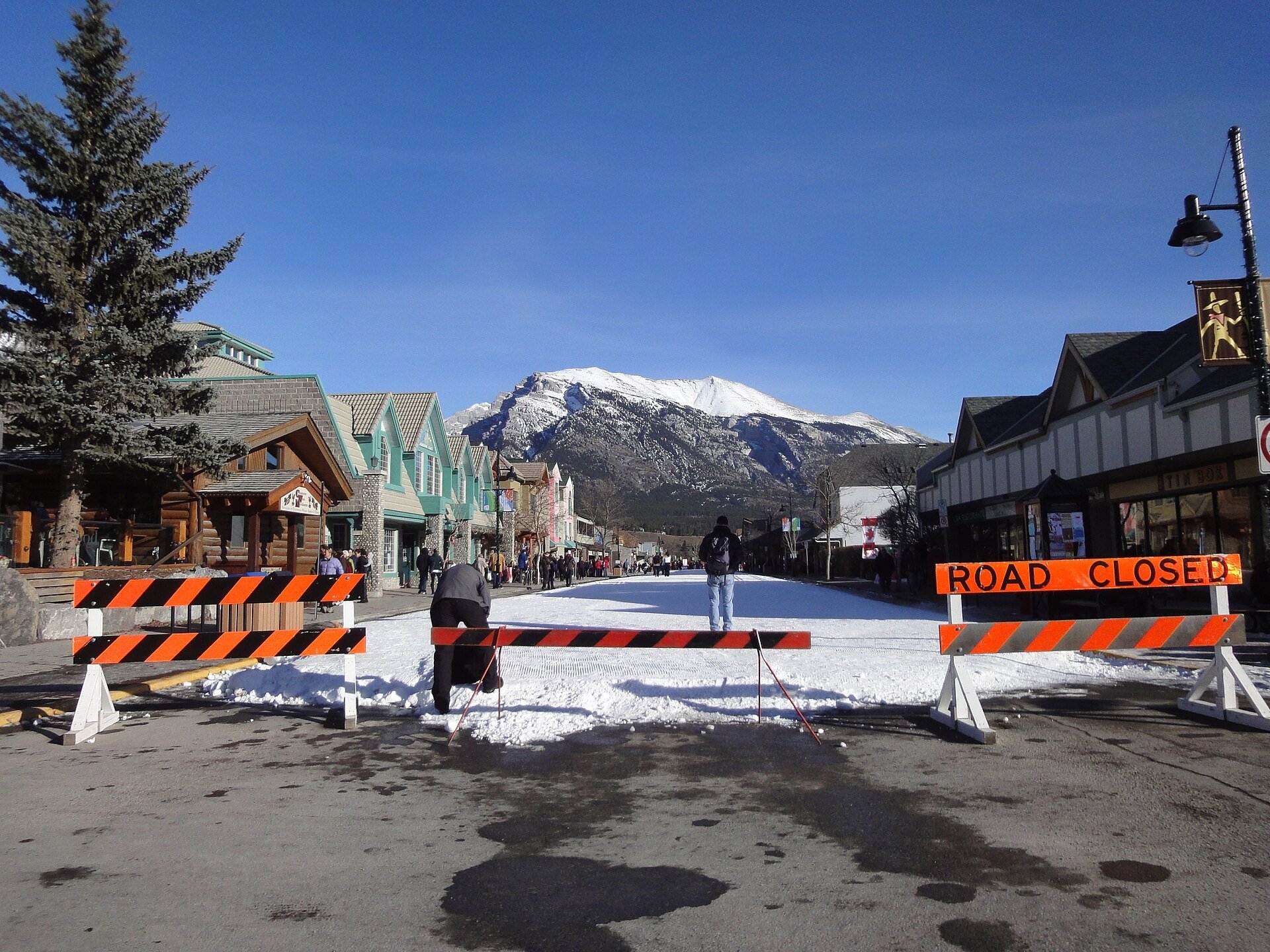 Snow on Main Street in downtown Canmore with mountains behind the shops.