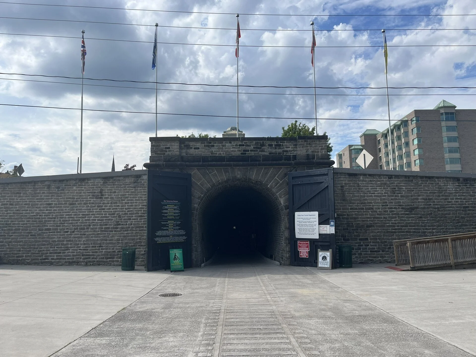 The stone south portal of the Brockville Railway Tunnel with flags flying above the entrance near the waterfront.