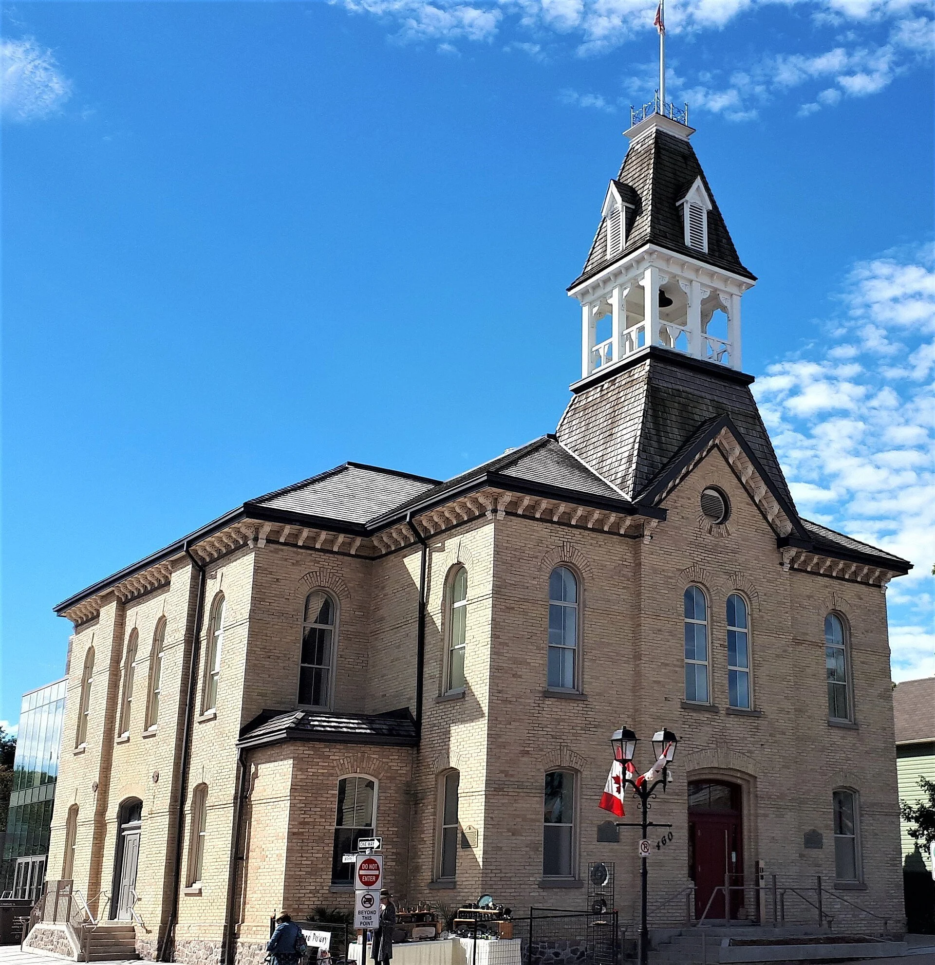 Newmarket's 1883 Old Town Hall on Botsford Street, a buff brick building with a white cupola under a bright blue sky.