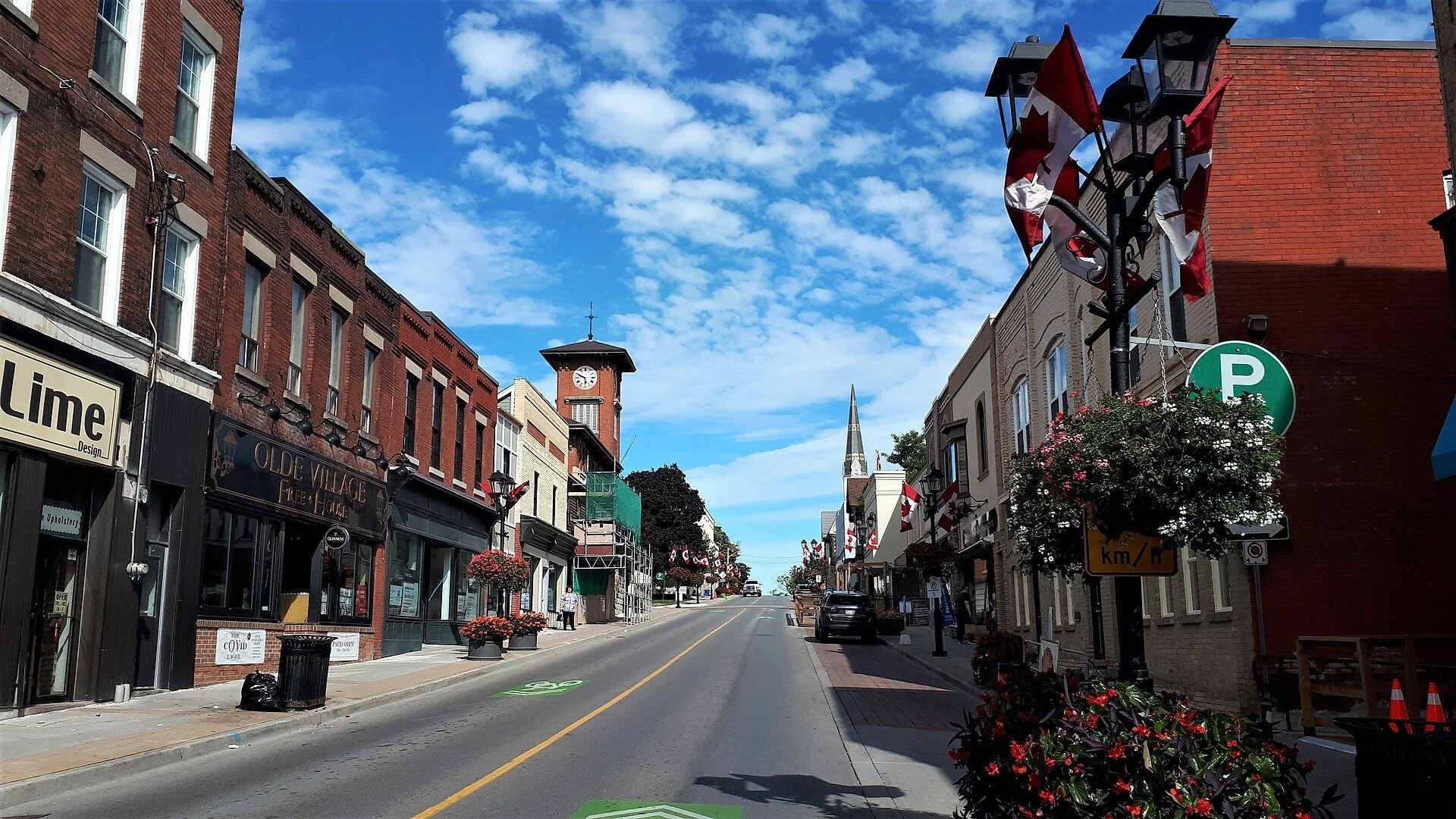 Historic brick storefronts with hanging flower baskets and Canadian flags along Main Street South in downtown Newmarket.