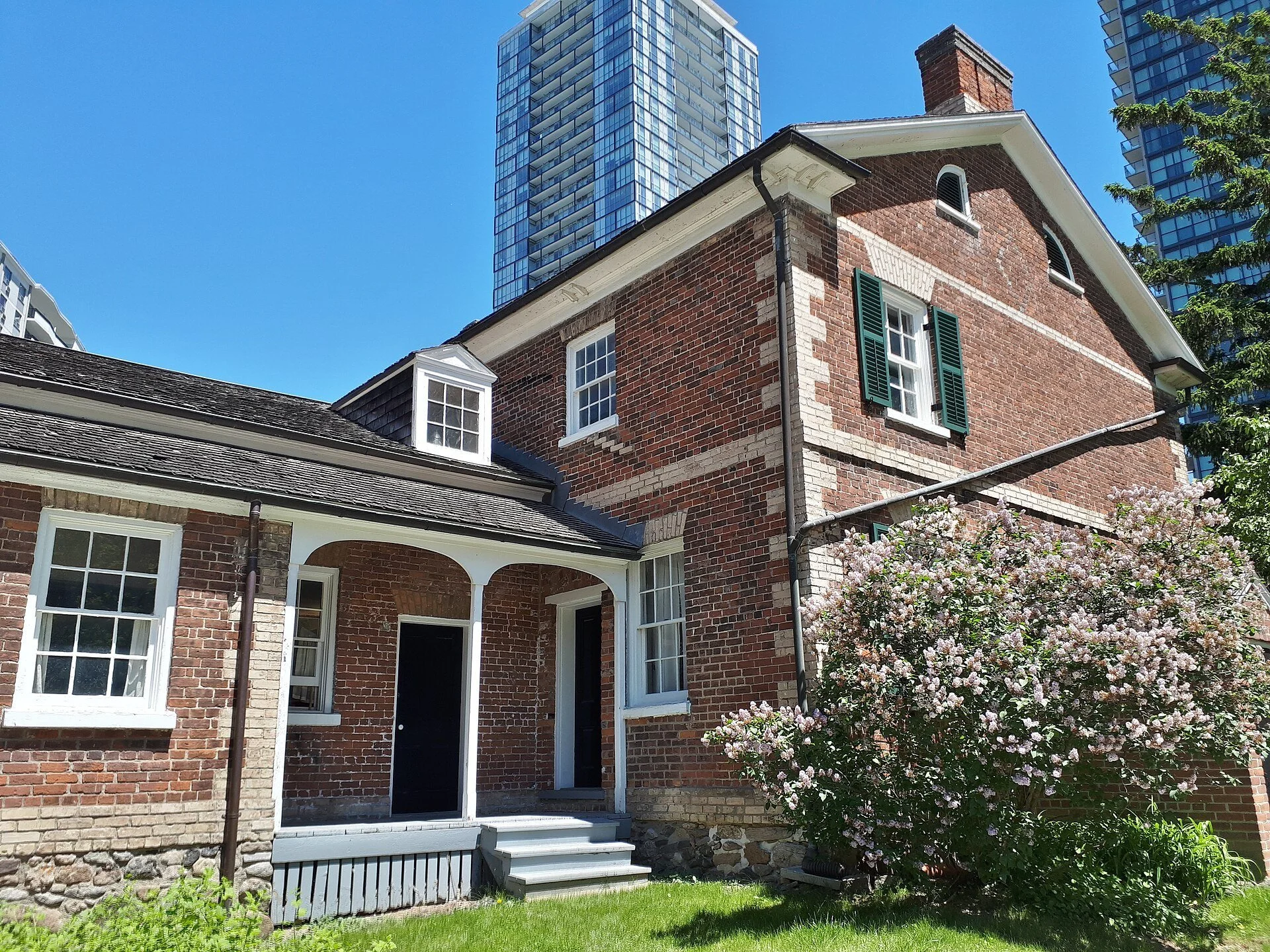 The rear of the red brick Gibson House in North York with a lilac bush in bloom.
