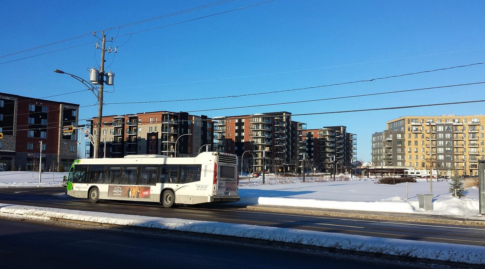 A city bus passes new apartment buildings along a snowy street in Blainville, Quebec.