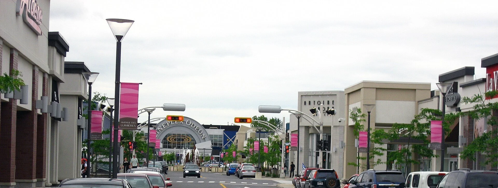 A pedestrian-friendly street of shops and restaurants lined with lamp posts and banners at Quartier DIX30 in Brossard.