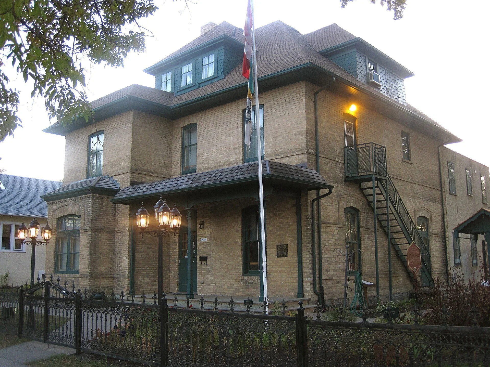 The brick Daly House Museum in Brandon with its iron fence, garden lamps and a flag out front.