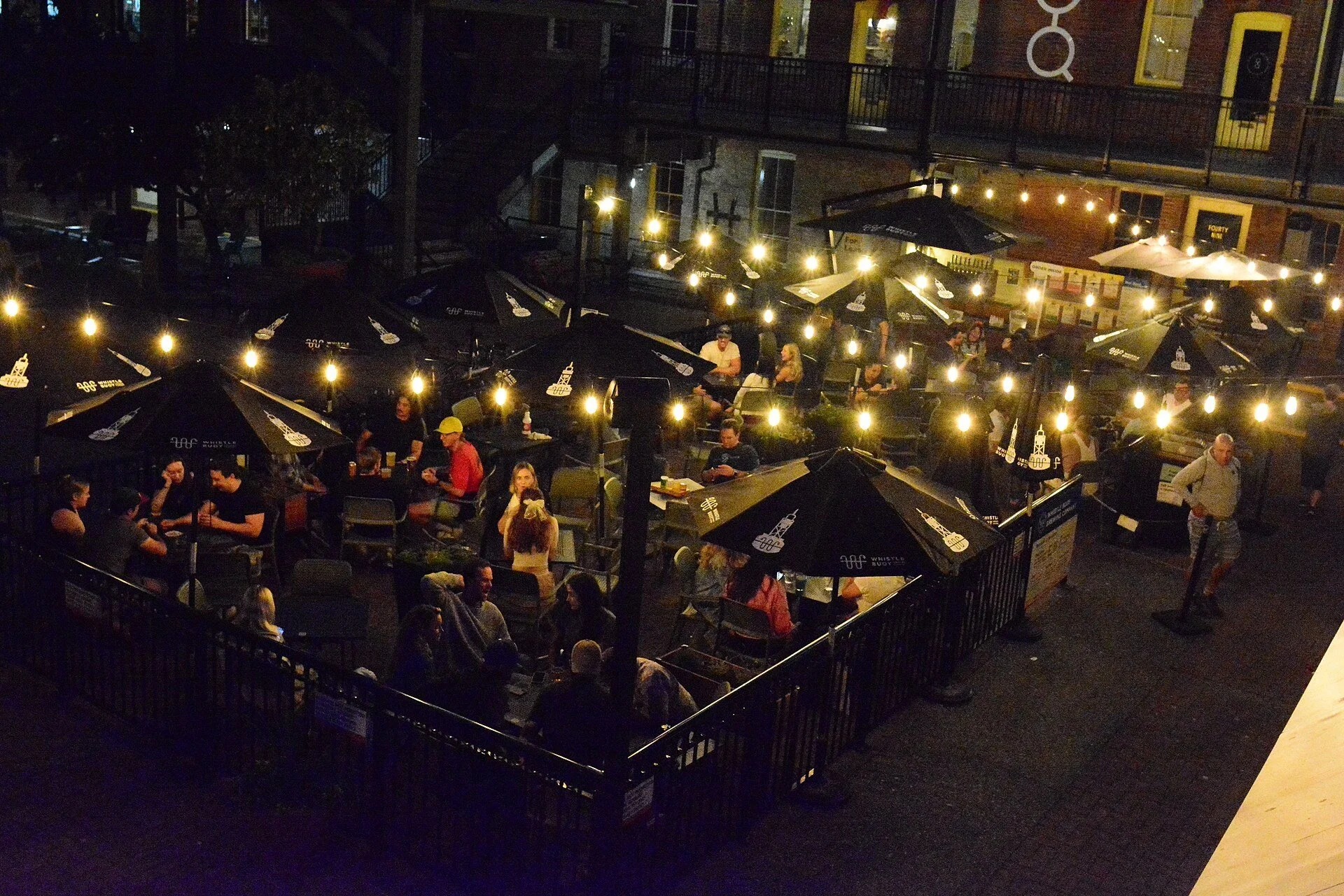 String lights over the courtyard patios of Market Square in Victoria at night.