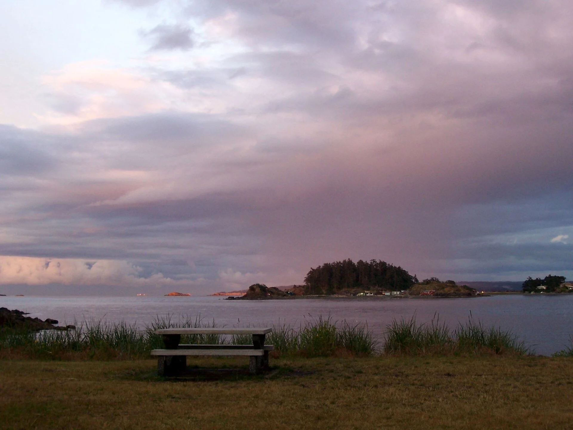 A picnic table on the shore at Neck Point Park looking toward Shack Island at dusk.