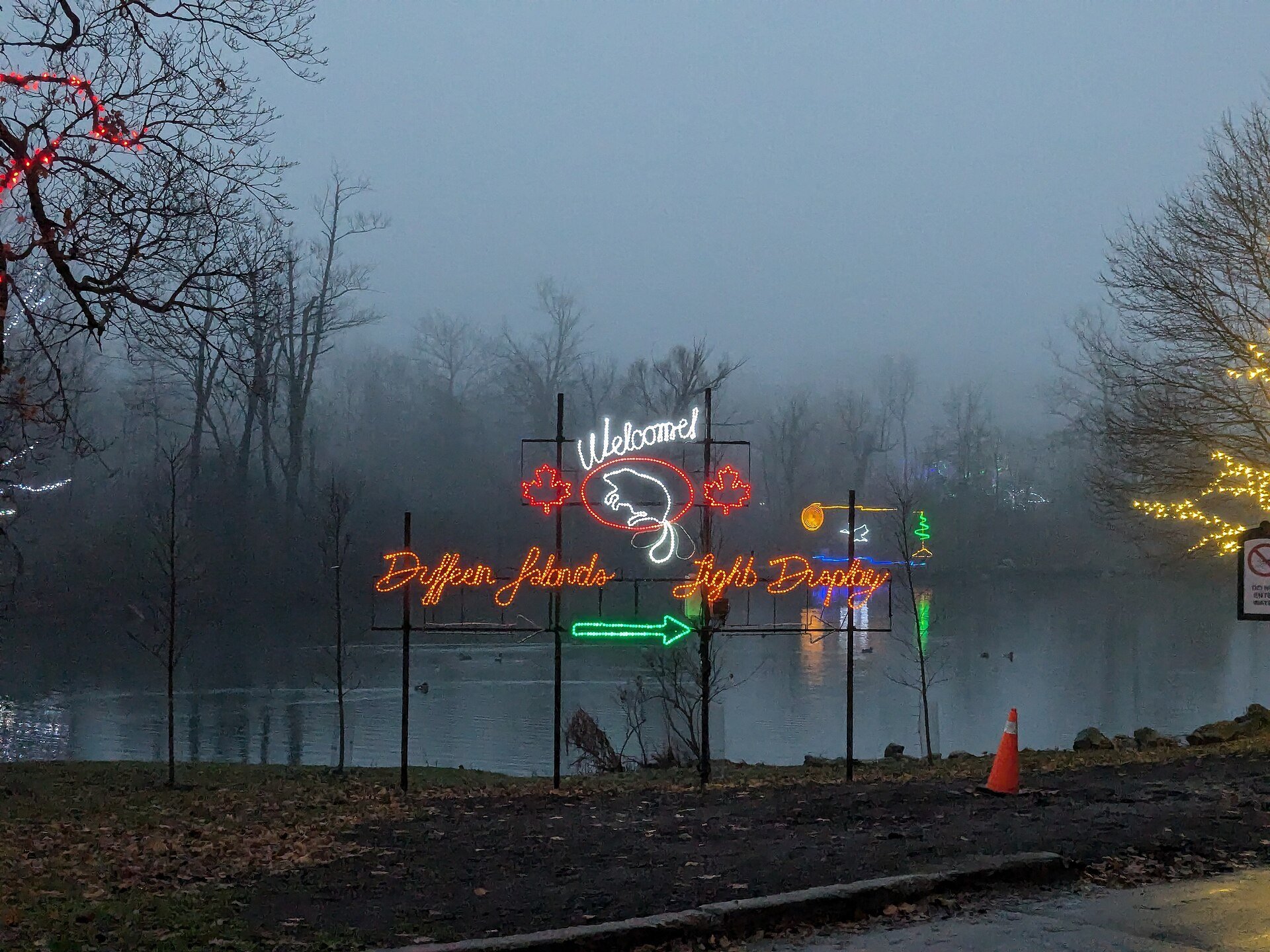 A lit welcome sign for the Dufferin Islands light display beside the water on a misty evening during the Winter Festival of Lights.
