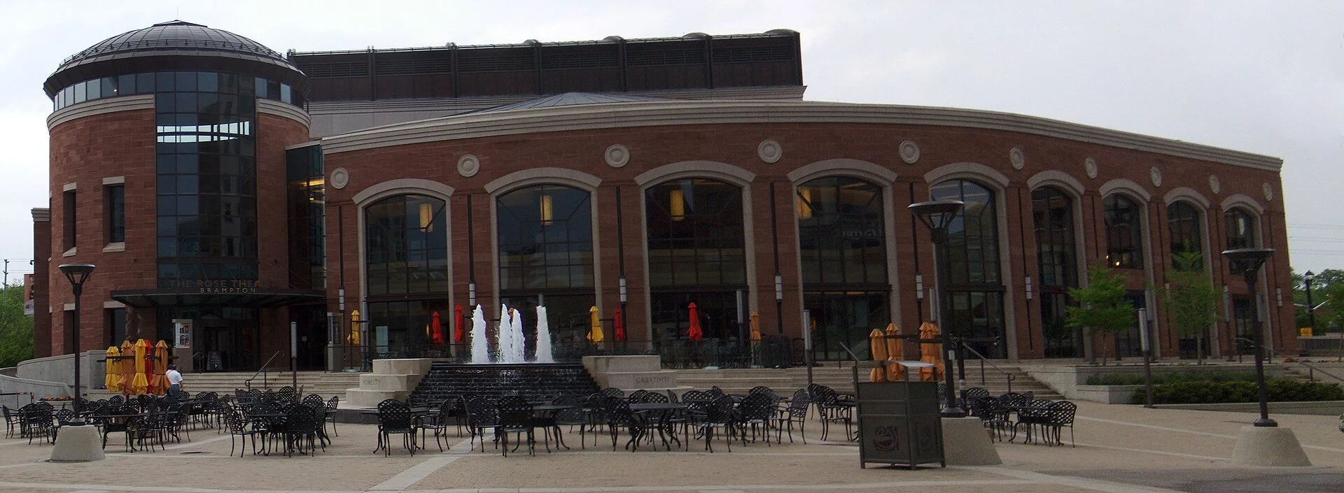 The curved brick front of The Rose theatre in downtown Brampton, with a fountain and patio seating in the square.