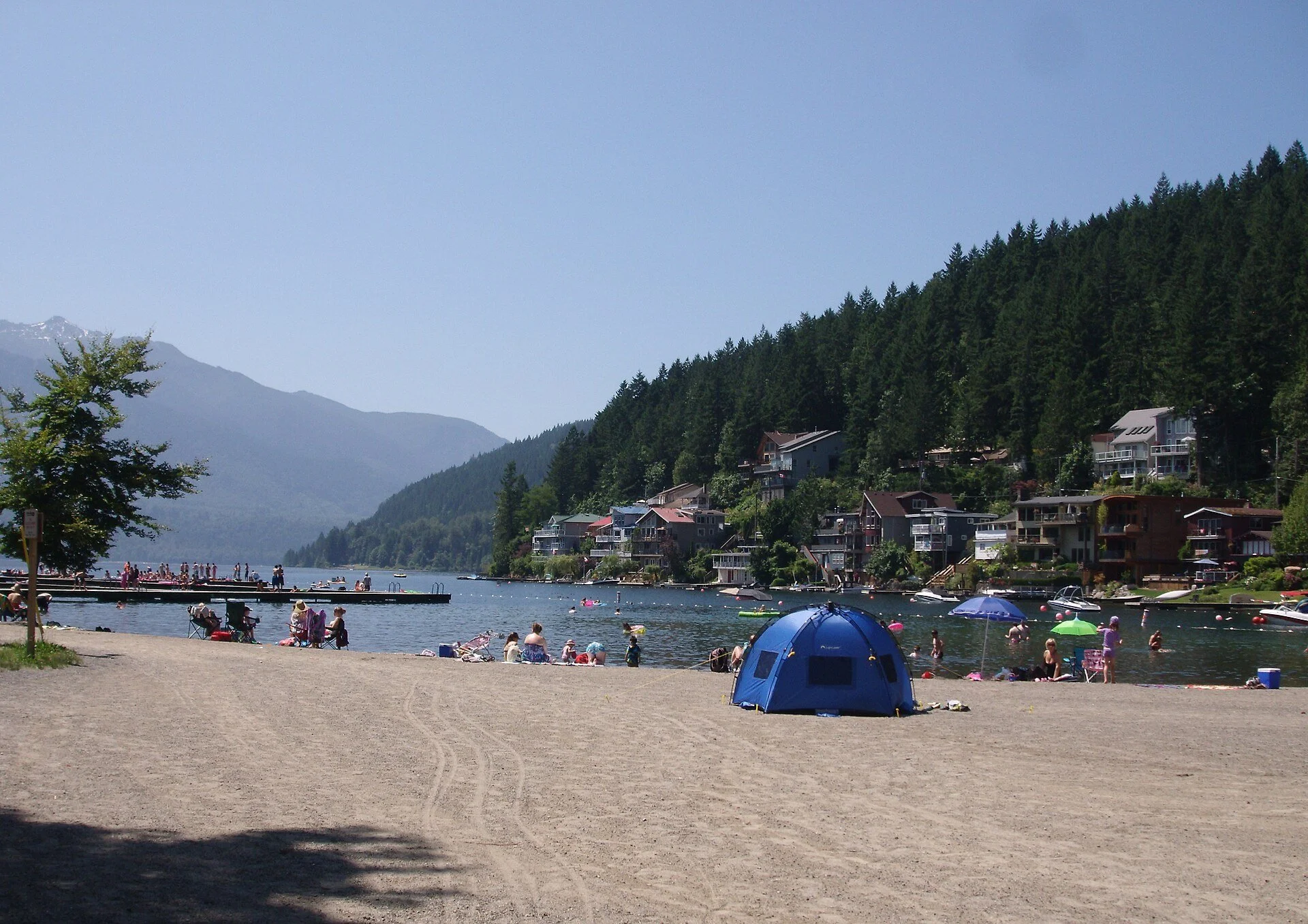 The beach at Cultus Lake with forested mountains behind it.