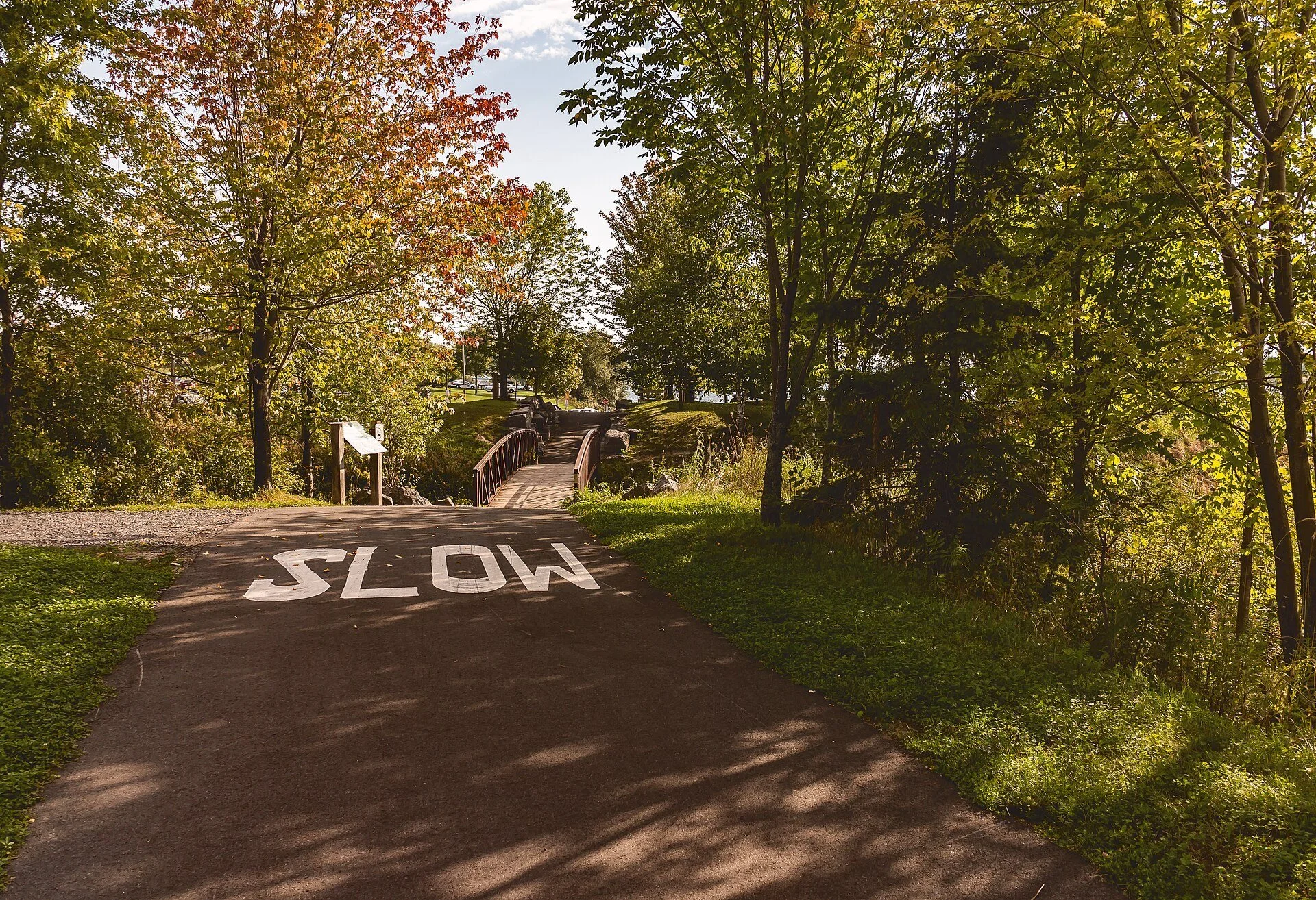 A paved path marked SLOW curving through trees with early fall colour in Lamoureux Park, Cornwall.
