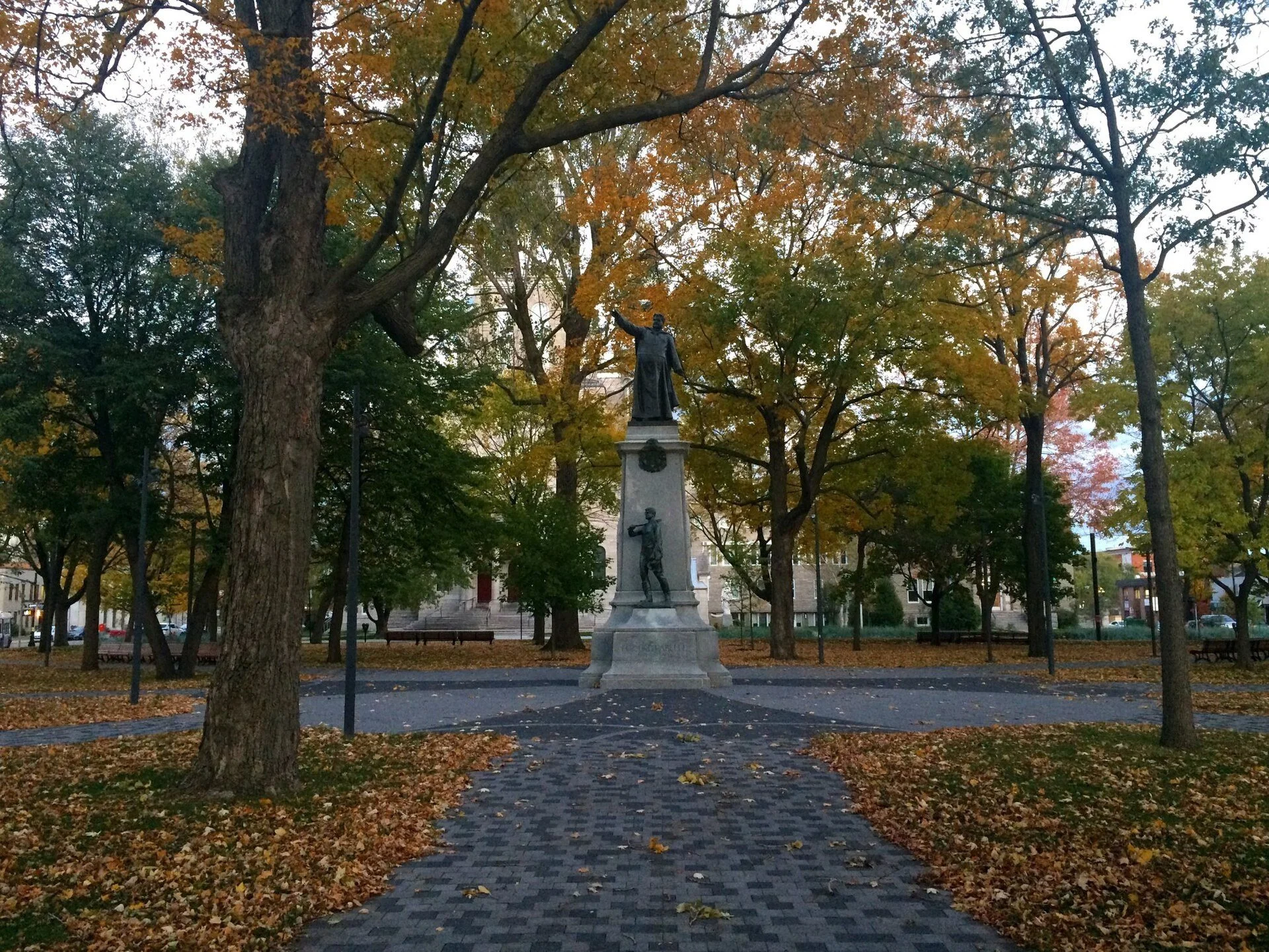 Autumn trees and fallen leaves around the statue of curé Labelle in Parc Labelle, downtown Saint-Jérôme.