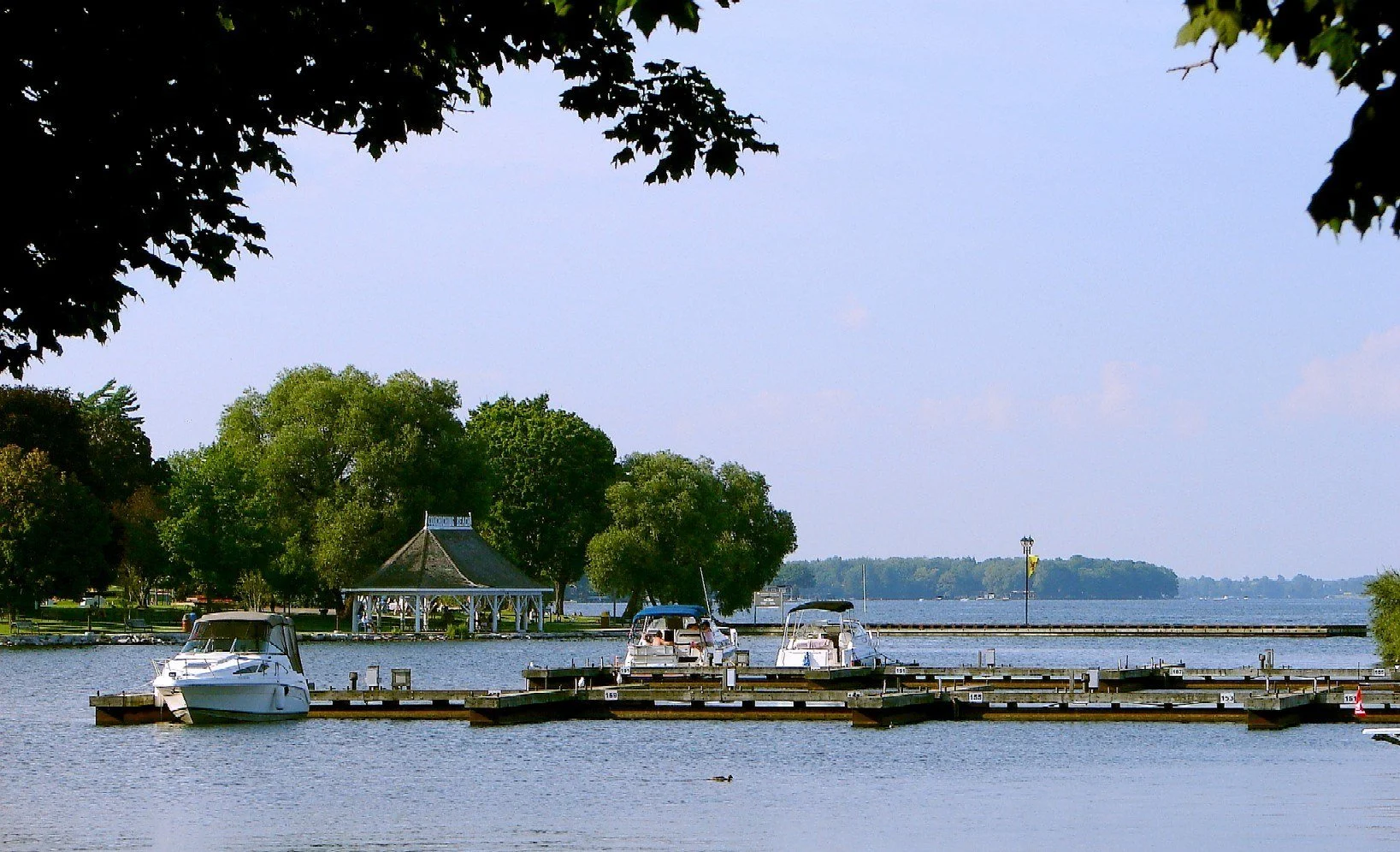 Boats at the docks on Lake Couchiching with a gazebo and leafy trees along the Orillia waterfront.
