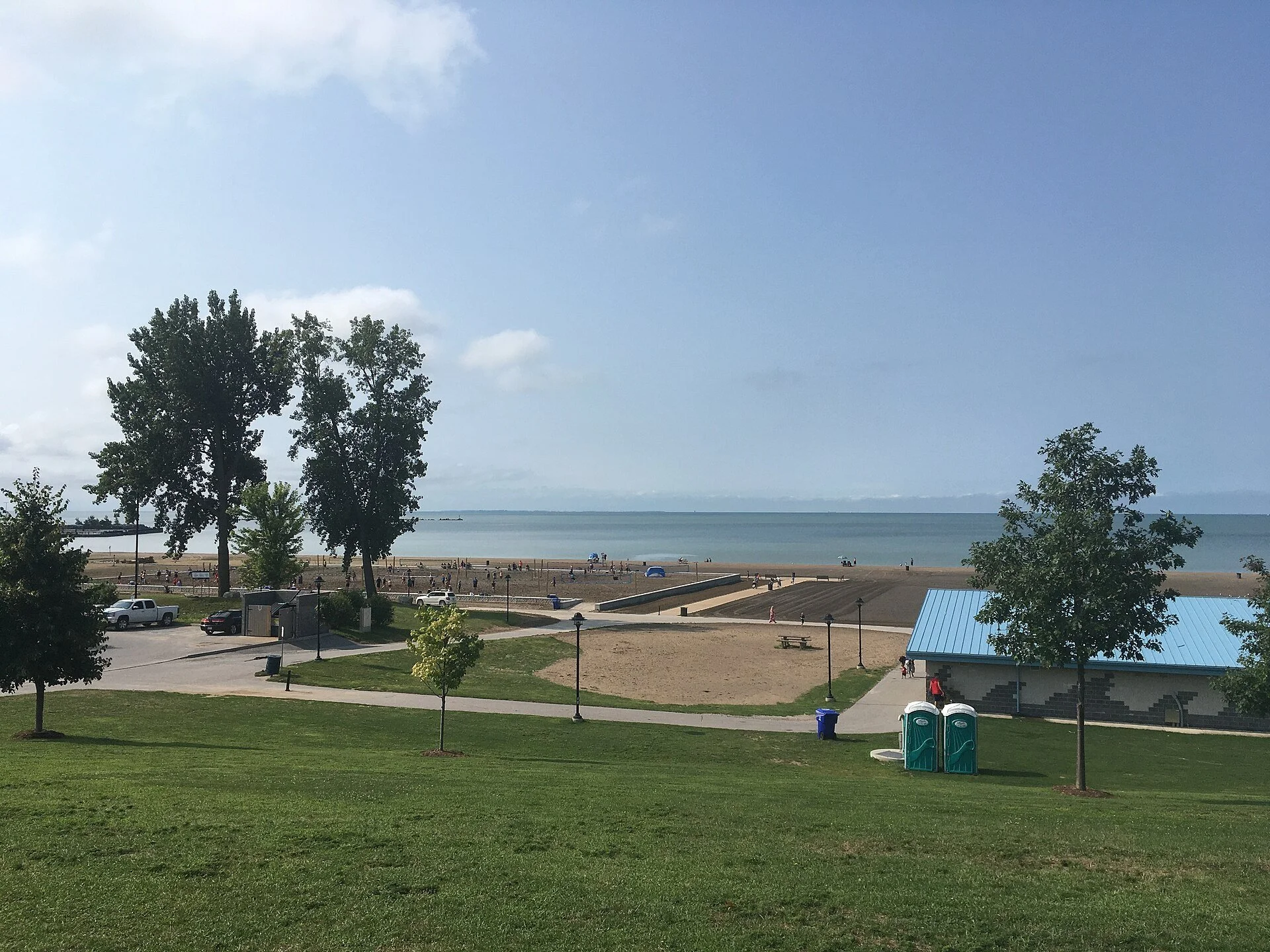 A grassy slope in Seacliff Park looking out over paths, trees and the calm water of Lake Erie in Leamington.