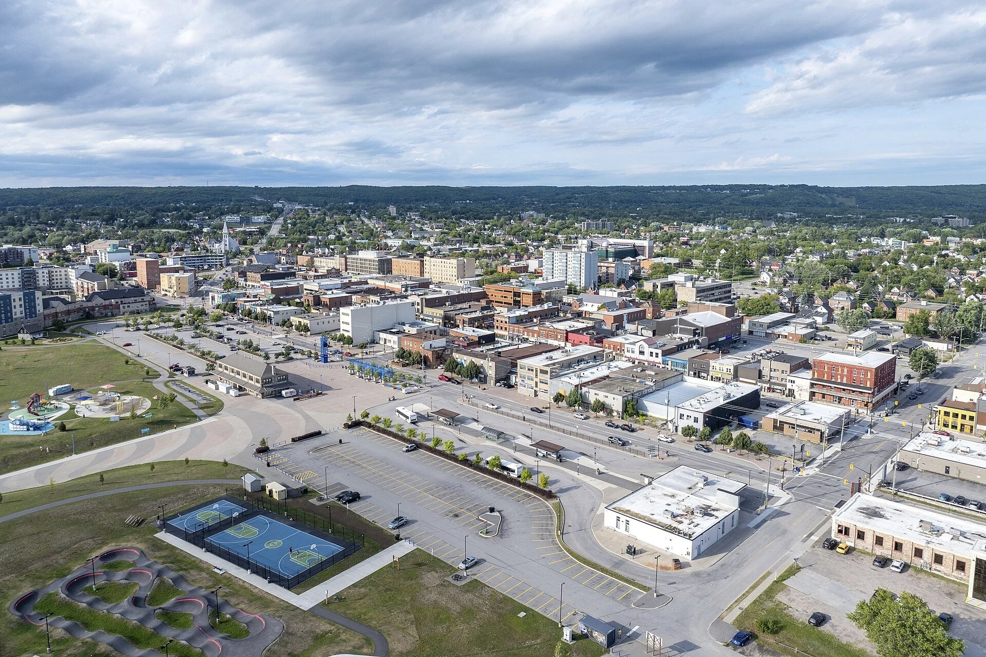 An aerial view over downtown North Bay, showing the waterfront parkland, parking areas and the downtown blocks.