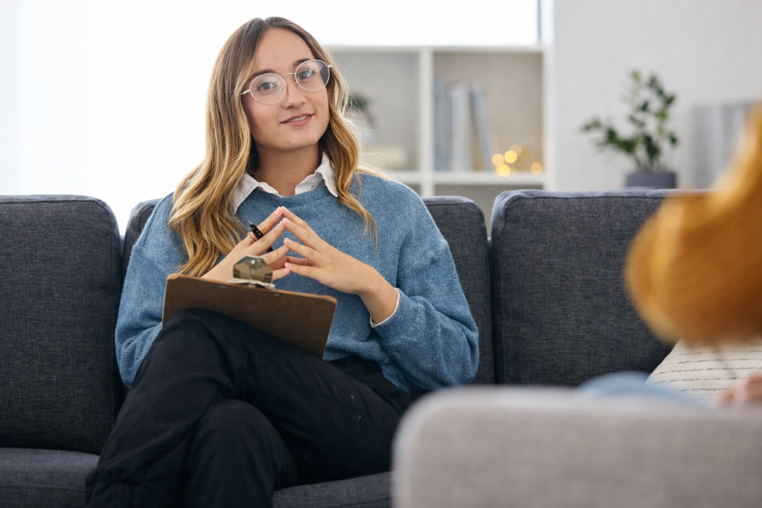 female ocd psychologist with glasses sitting on a couch in an assessment looking at the camera with her fingers pressed together