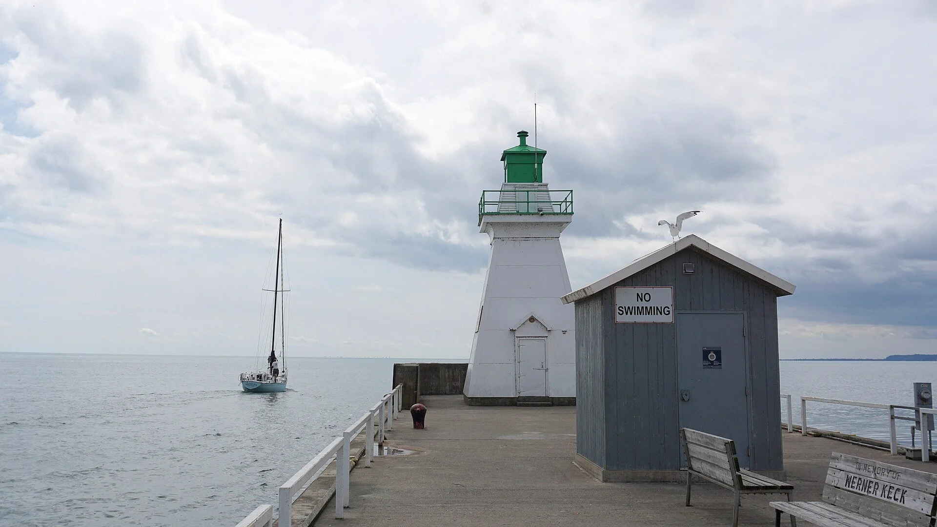 The white lighthouse at the end of the pier in Port Dover, with Lake Erie and a sailboat beyond.