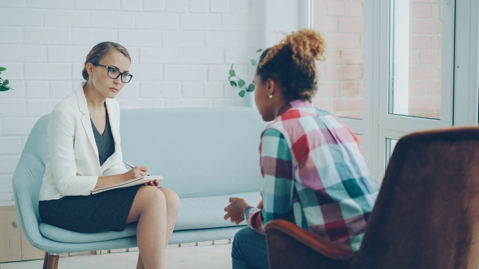 A psychologist listens closely and takes notes while an adult client speaks during a counselling assessment session.