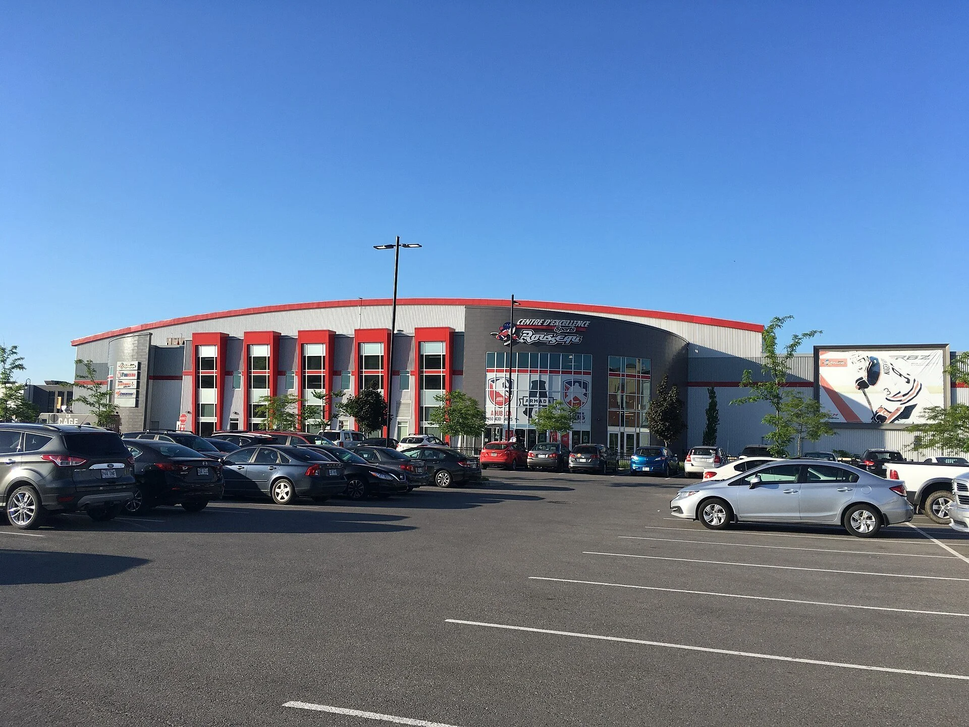 The Centre d'excellence Sports Rousseau arena and its parking lot on a sunny day in Boisbriand, next to Blainville, Quebec.