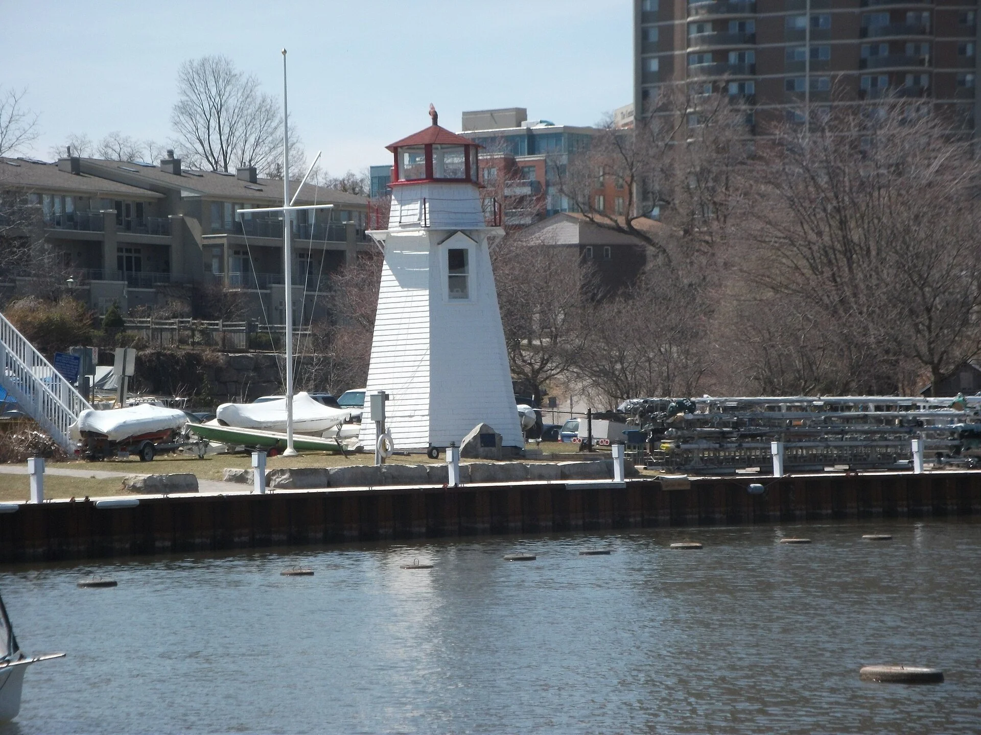 A white lighthouse with a red top beside the water at Oakville Harbour.