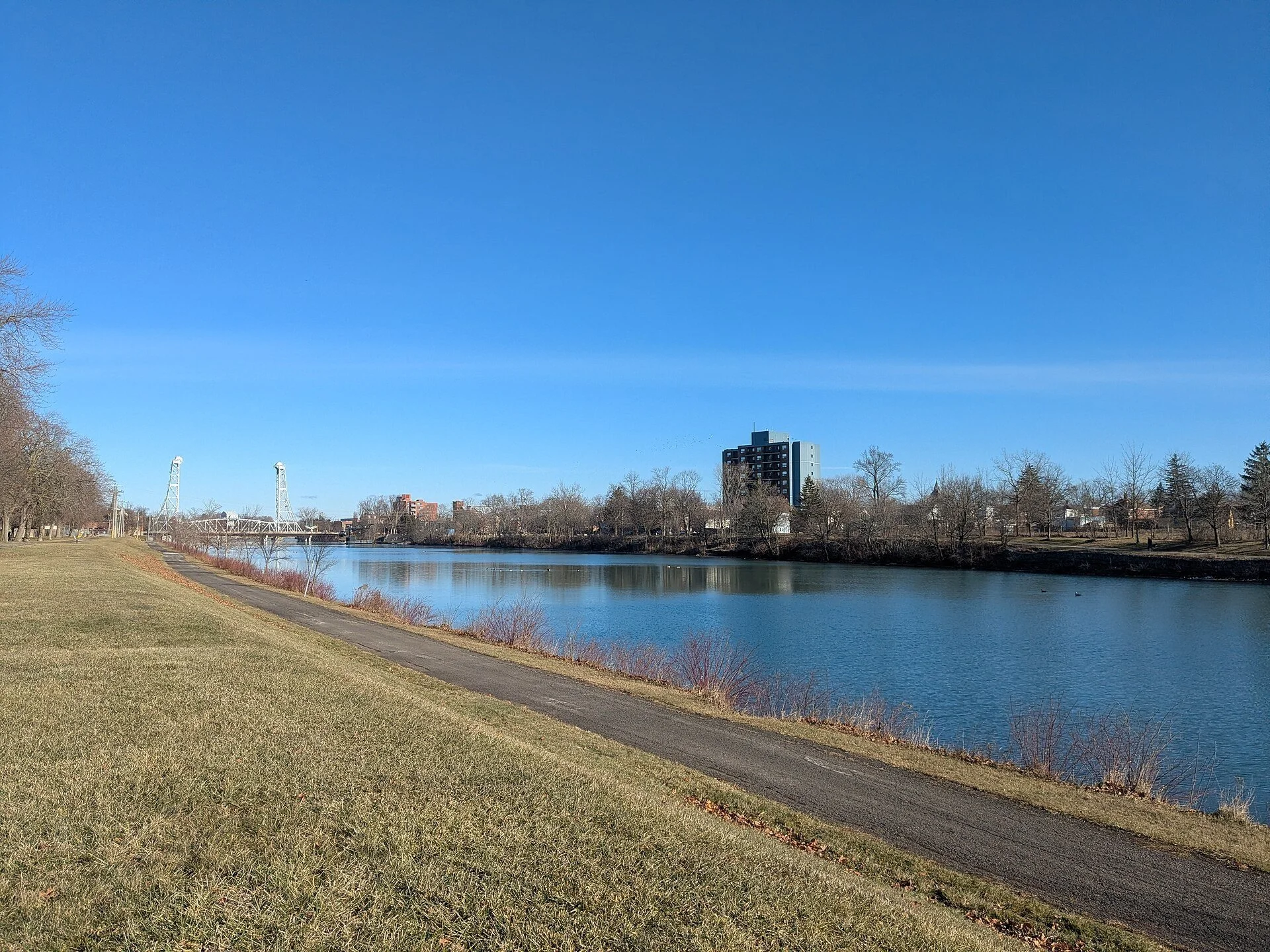 The still water of the Welland Recreational Waterway with a grassy path along its bank under a clear blue sky.