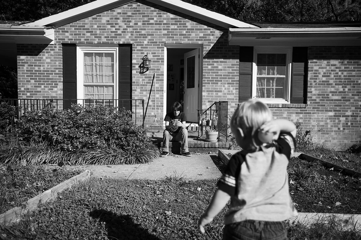 Arielle waits outside for her daughter and sister to arrive home from school while her son Dominique plays in the yard. 