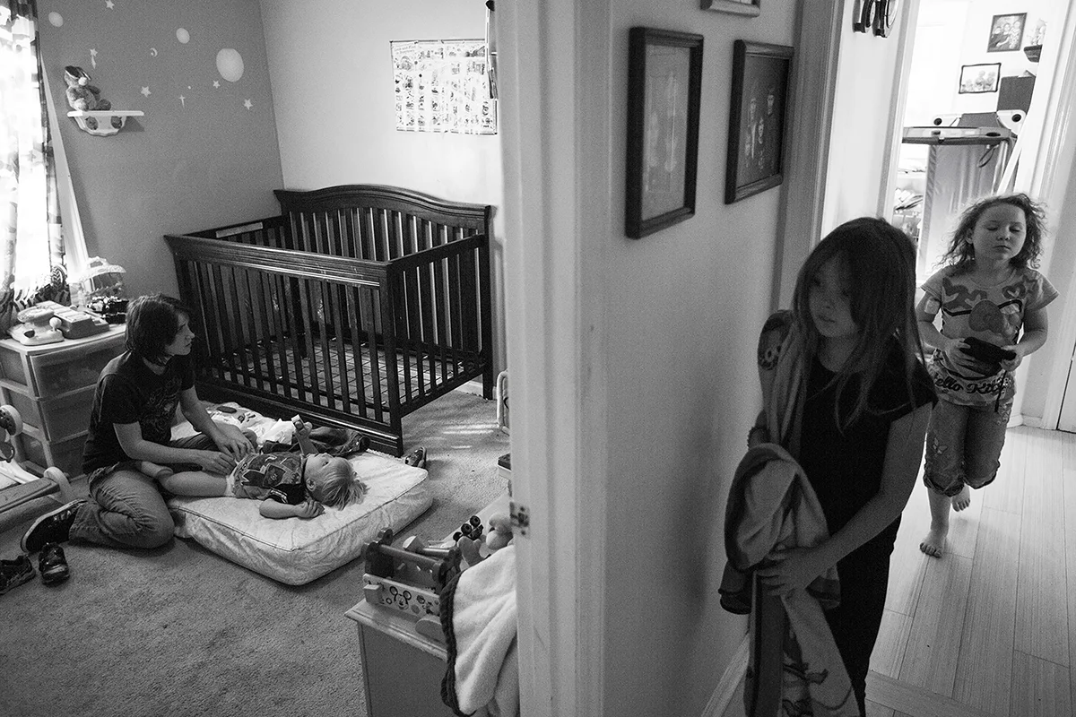  Arielle changes Dominique diaper in his room while Jazz, center, and Katana run down the hallway after getting home from school. 