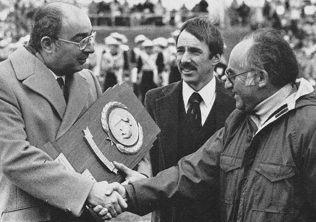 Coach Cy Fritz (right) and Assistant Coach Jeff Bradley (center) accepting the NCAA DII National Championship cross country trophy from MU President Joseph Caputo in 1981